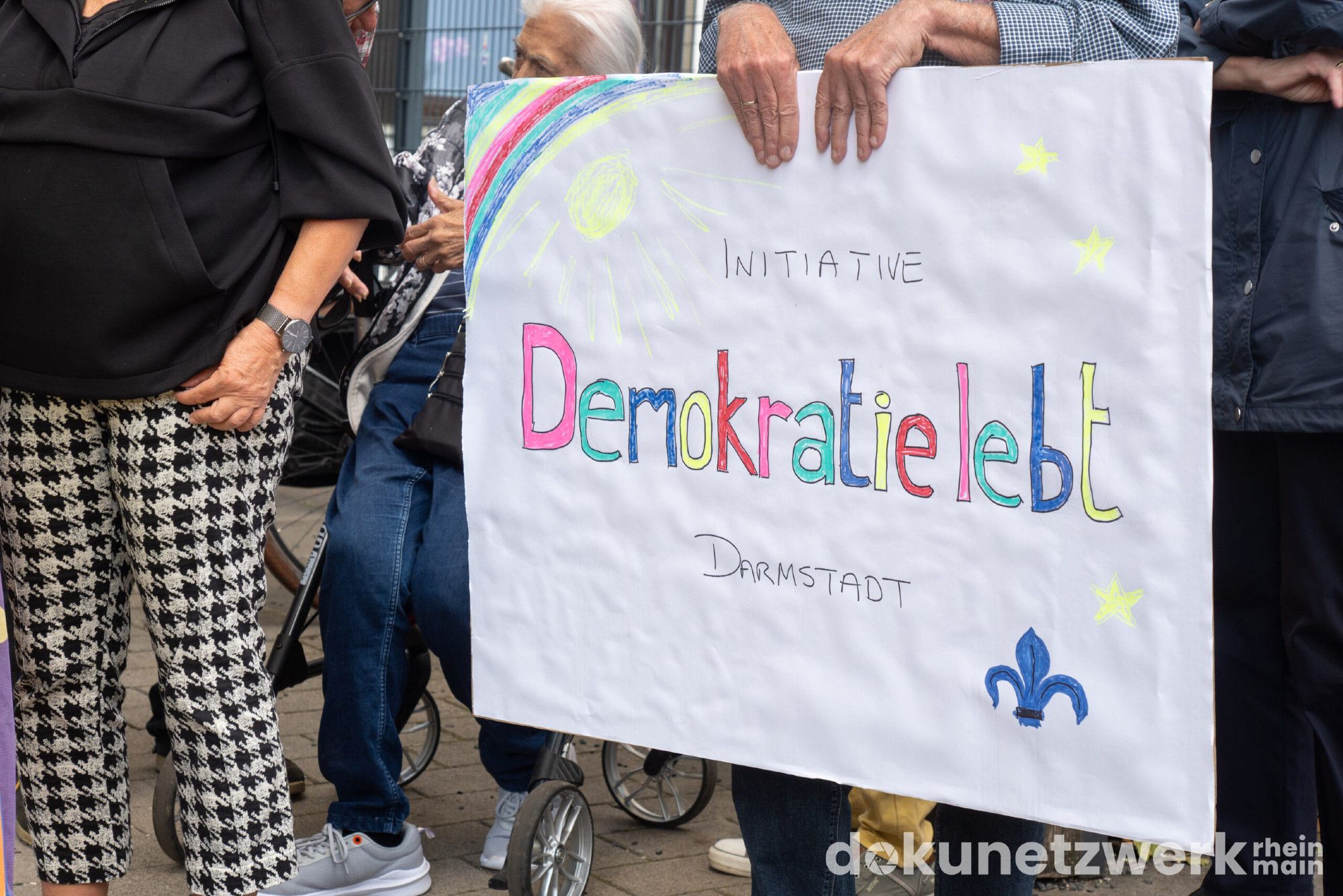 Ein weißes Schild worauf mit bunten Buchstaben steht: Initiative Demokratie lebt Darmstadt