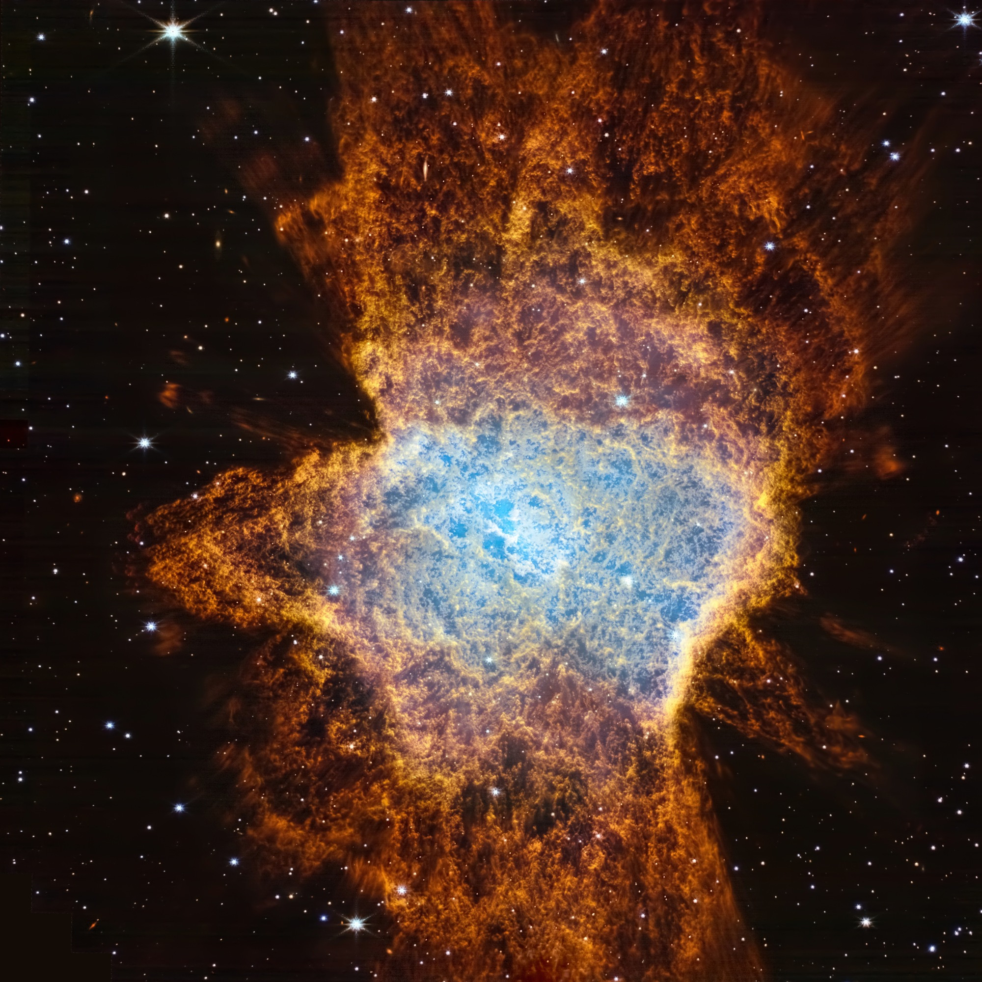 A JWST image of a planetary nebula shows a vivid, cloud-like structure in space. At the center, a brilliant electric blue core radiates intense light, surrounded by layers of orange and rusty red filaments that billow outward like expanding glowing smoke. The texture is rich and complex, with delicate wisps extending into the surrounding darkness. Countless stars and some galaxies dot the black background, contrasting sharply with the vibrant, detailed cloud at the heart of the image.