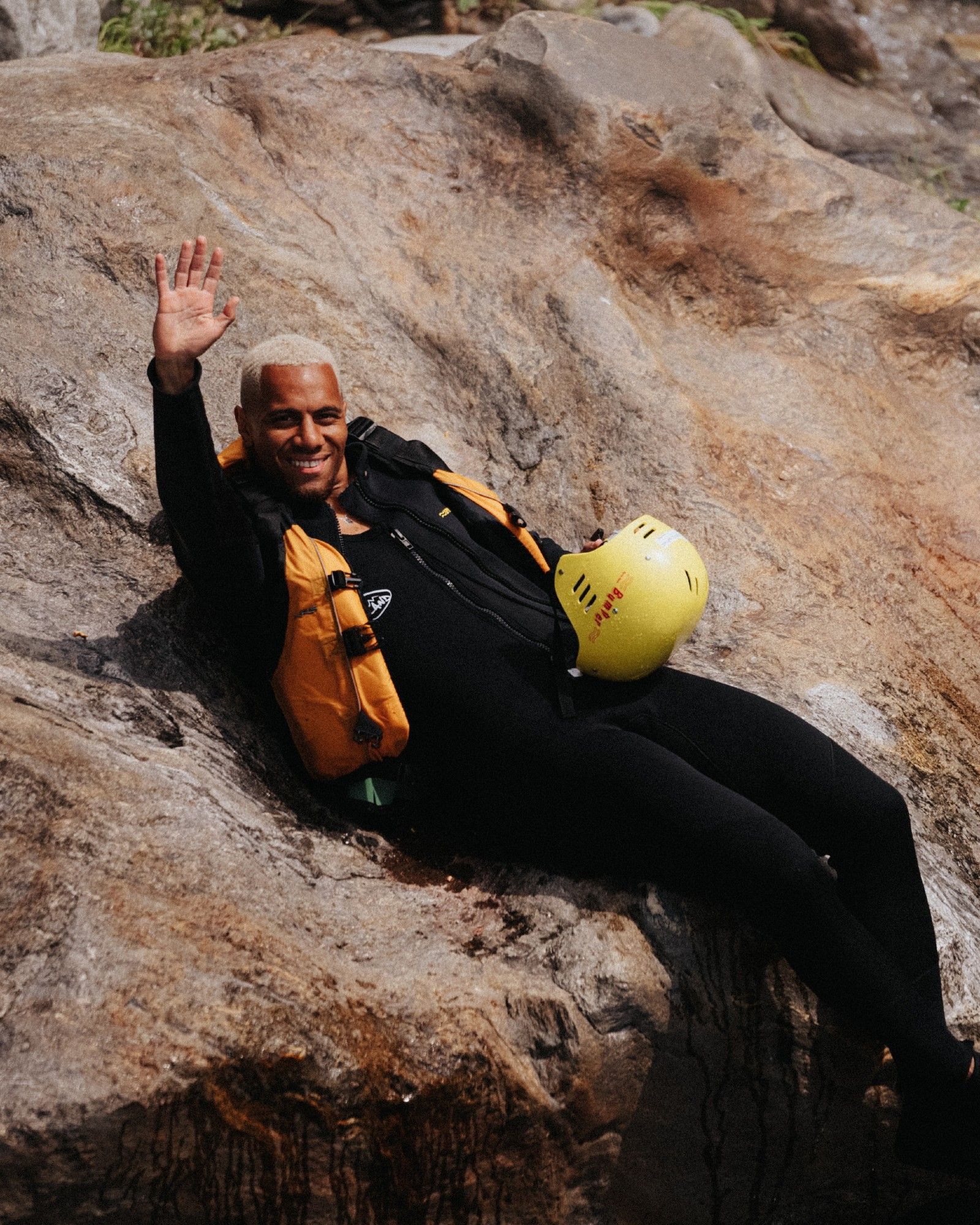 Etienne Amenyido winkt in Rafting-Bekleidung von einem Felsen aus.