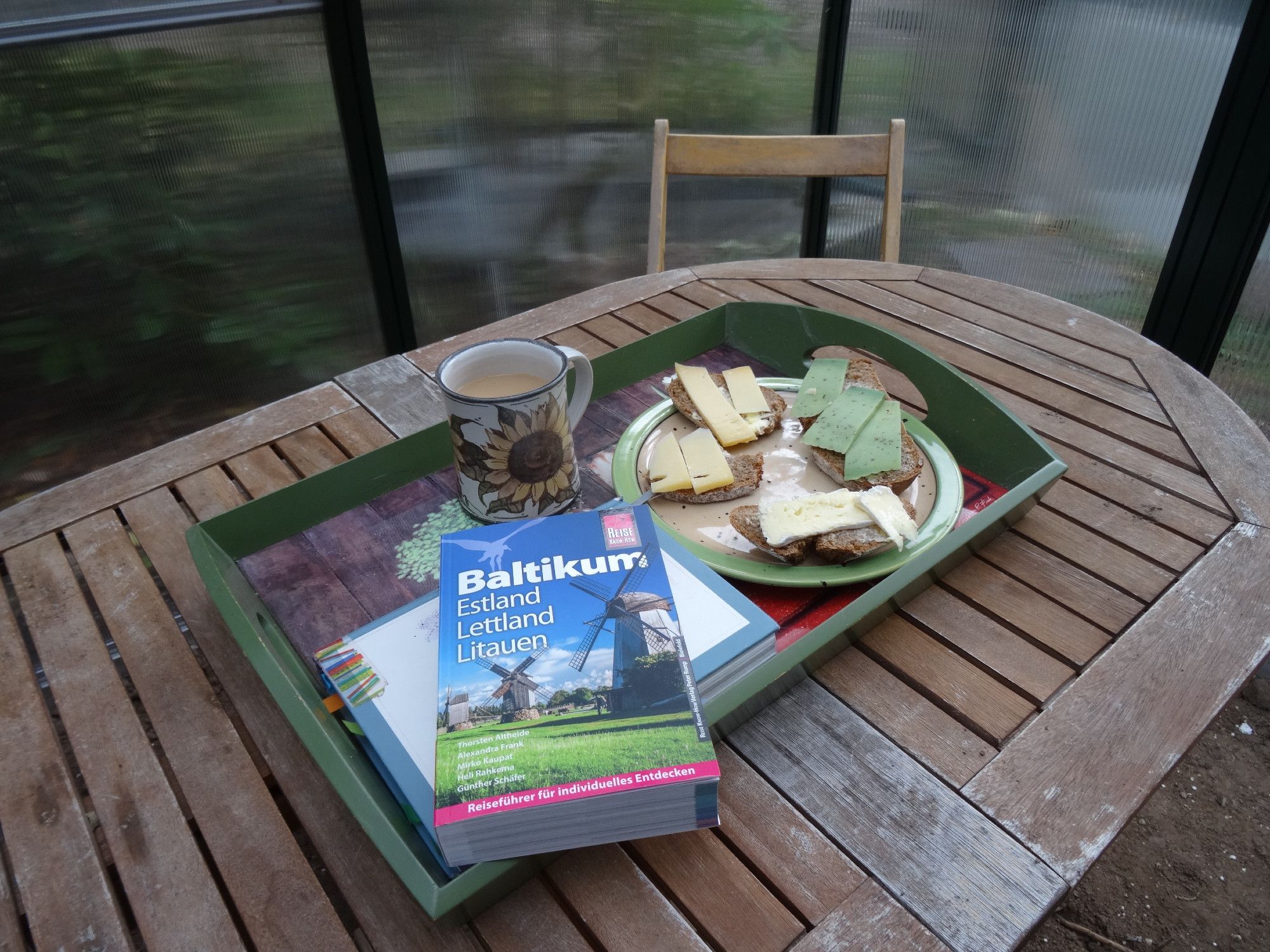 A tray on garden table in the new glasshouse with coffee, books and cheese-bread slices