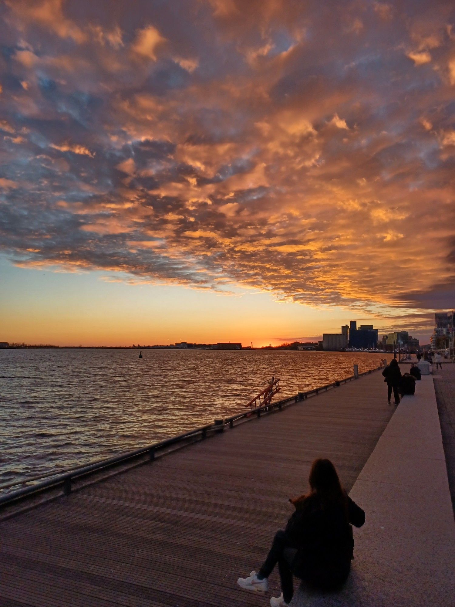 Photo of Lake Ontario at sunset, with a visible boardwalk, blue/pink skies, and the light reflected on the lake