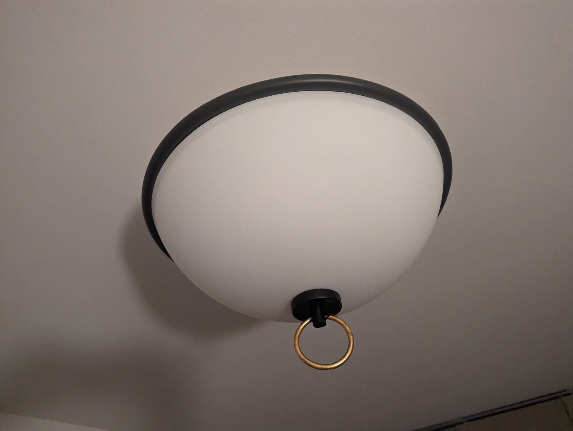 A round ceiling light with a big golden hoop hanging out of the bottom 