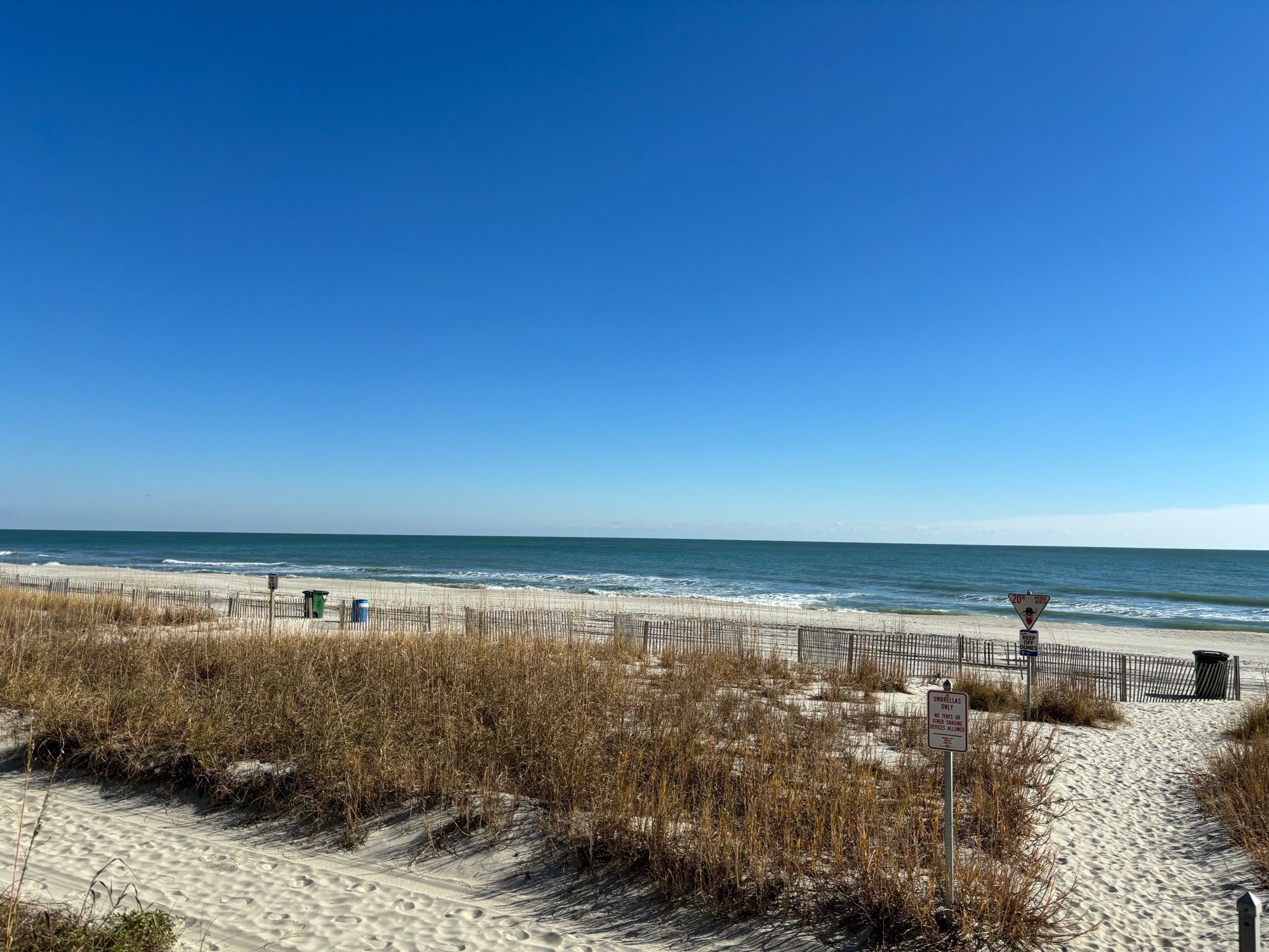 View of the ocean and beach. There are no people on the beach.  It has a beautiful blue sky.