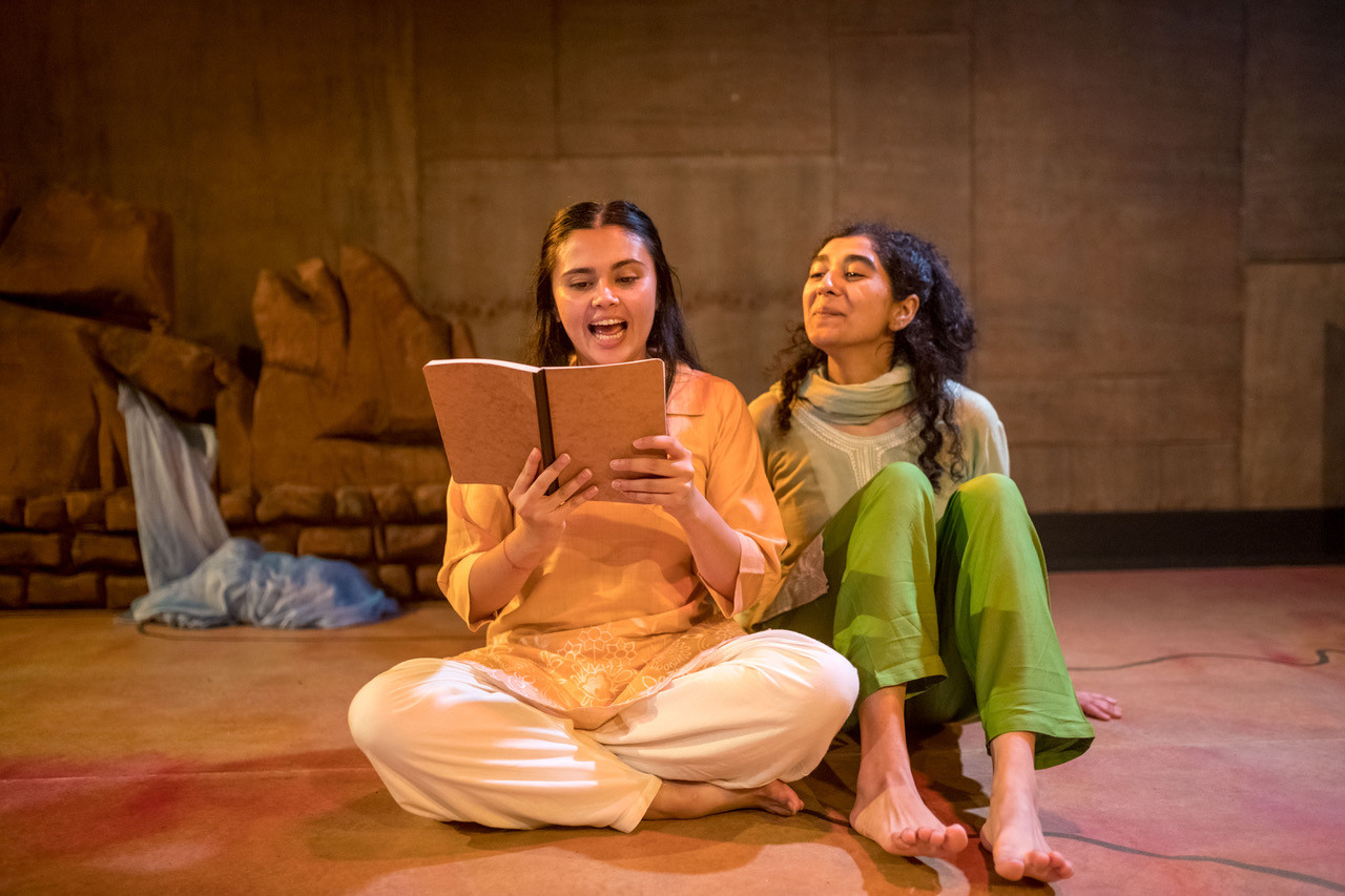 two female performers sat reading a book together