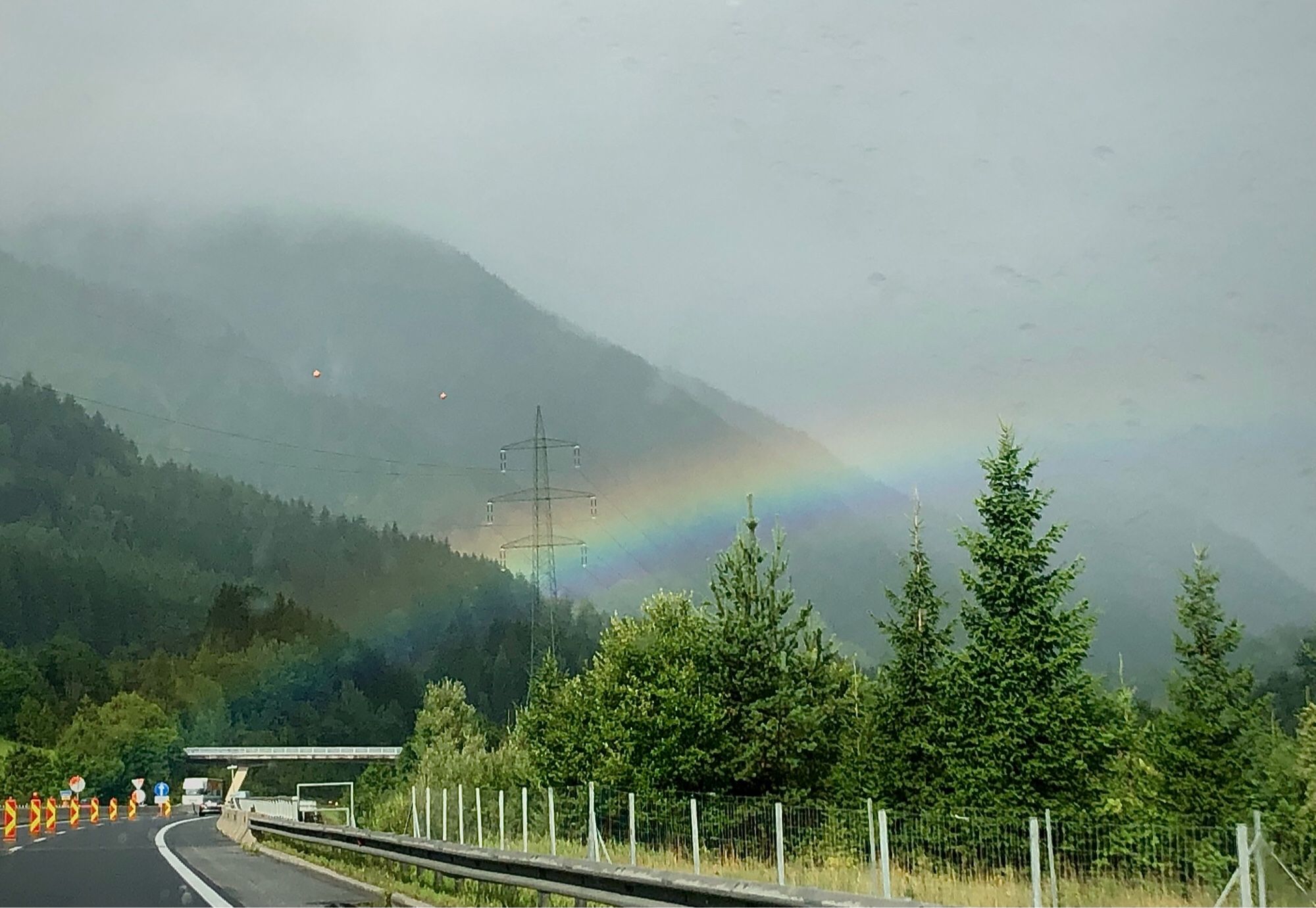 Regenbogen über österreichischer Autobahn , die auf Berge im Sprühnebel zufährt