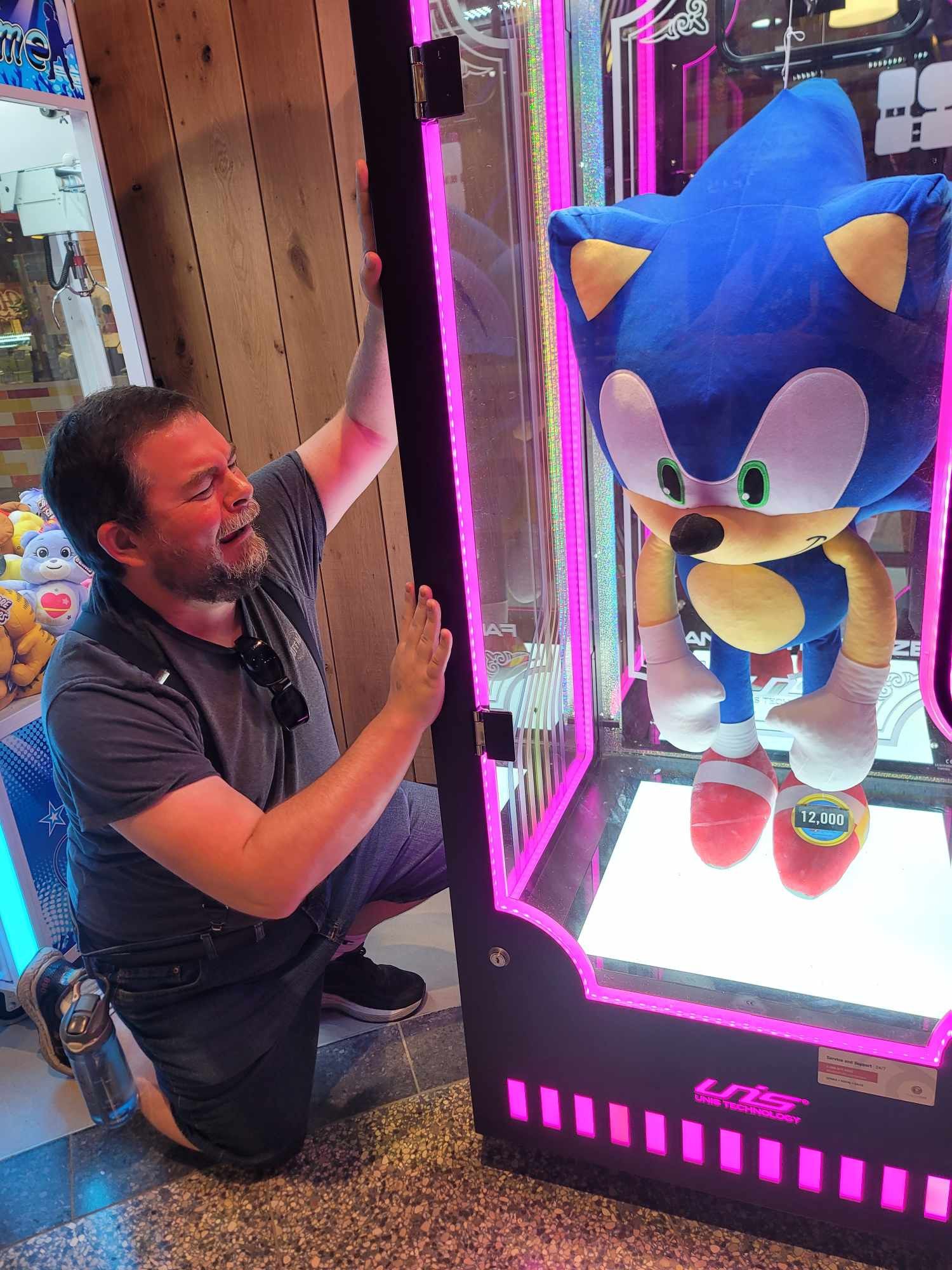 Ian Flynn melodramatically pounds on a glass case containing an oversized Sonic the Hedgehog plush doll.