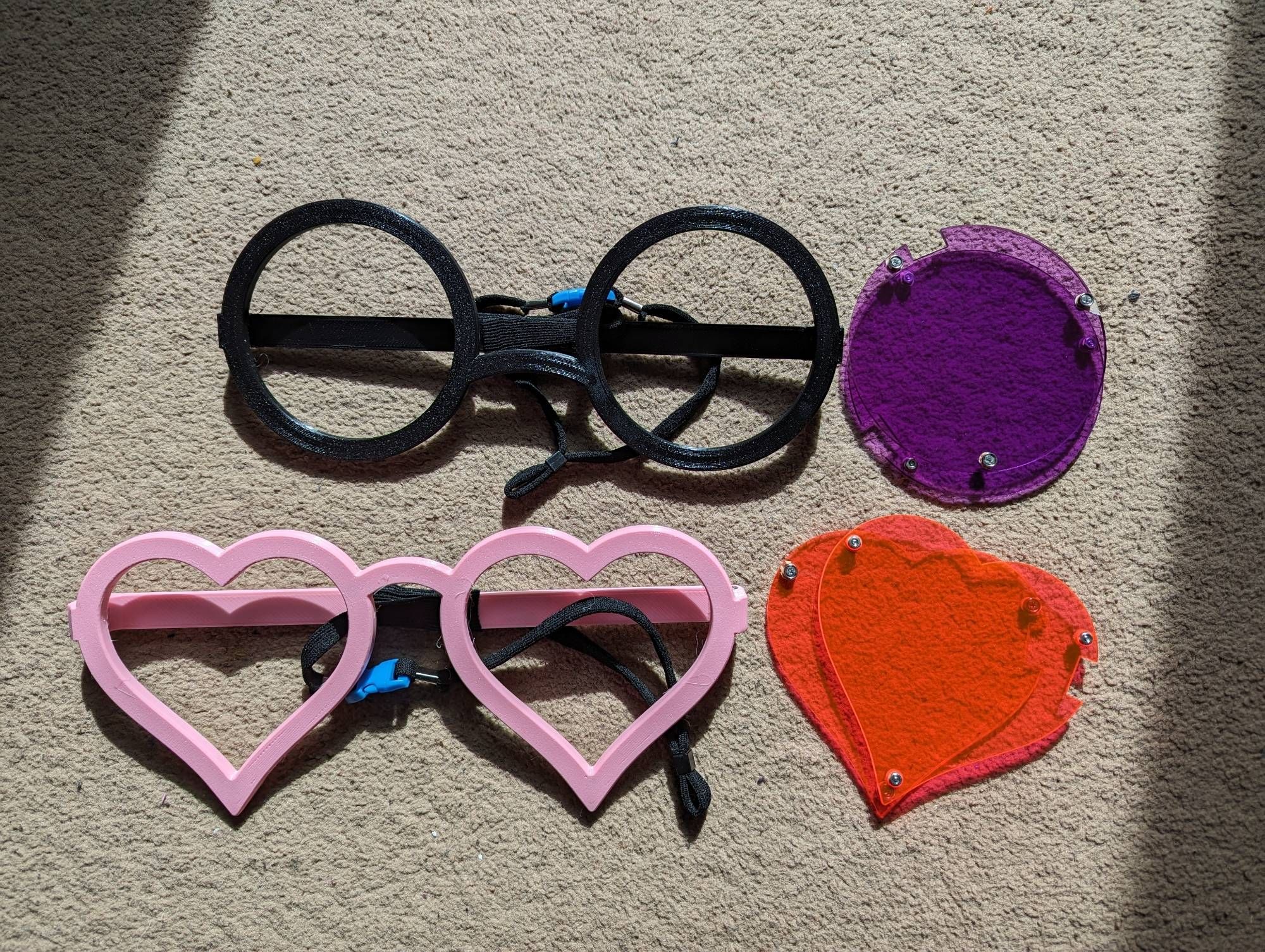 A pair of black circular glasses frames, and pink heart shaped frames, with purple circle and red heart lenses. They are oversized props intended to be used with fursuits.