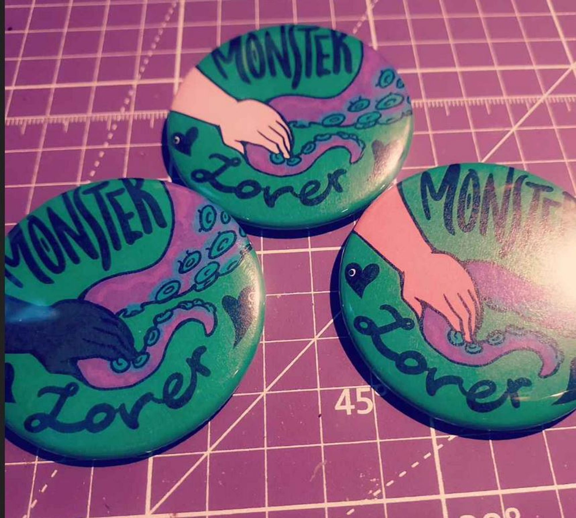 "Monster Lover" buttons, three of them with three different skin tones including Black, white, and brown, holding a purple and green tentacle lover's hand in each one.