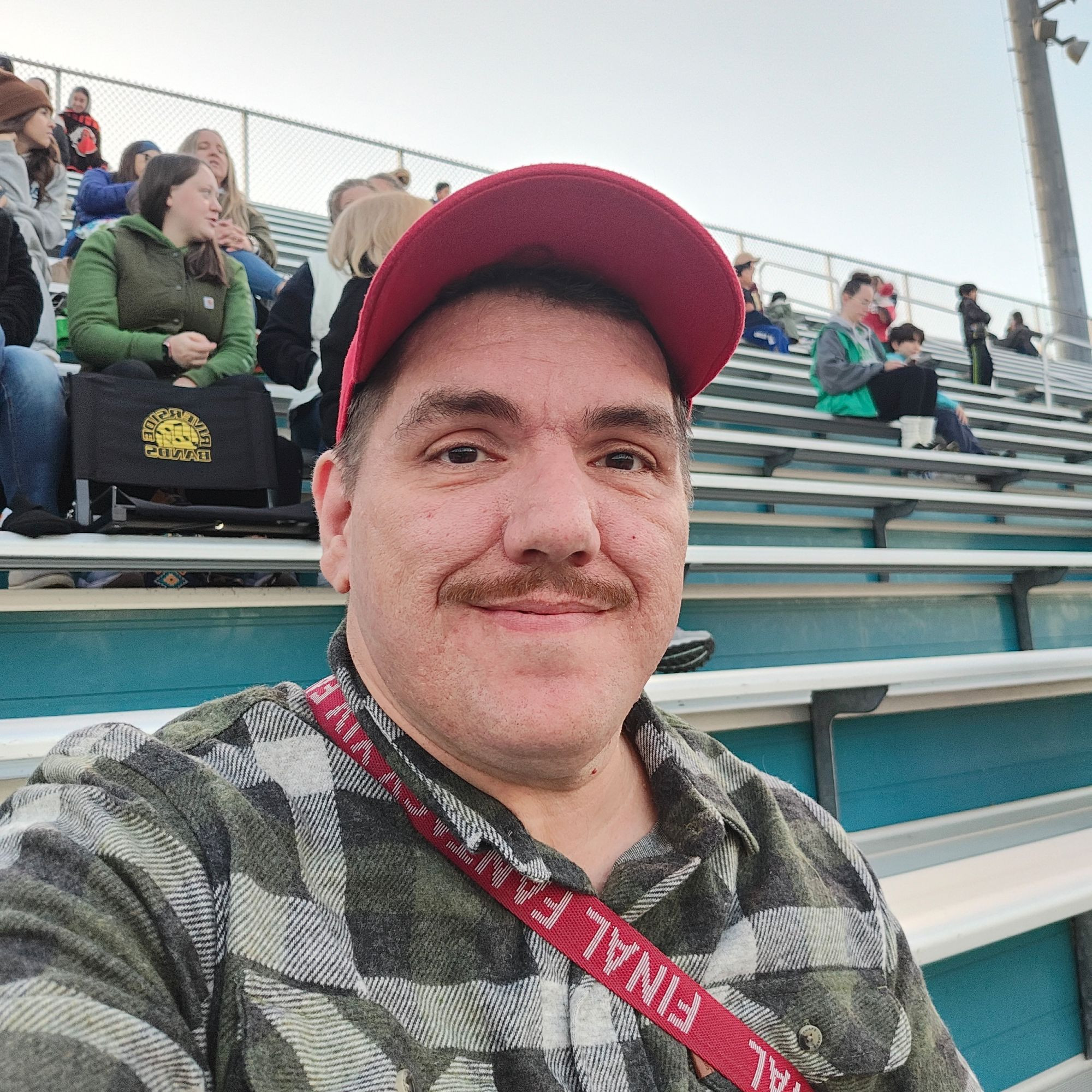 Me in a green flannel shirt and red baseball cap, sitting in the bleachers. What an absolute cutie.