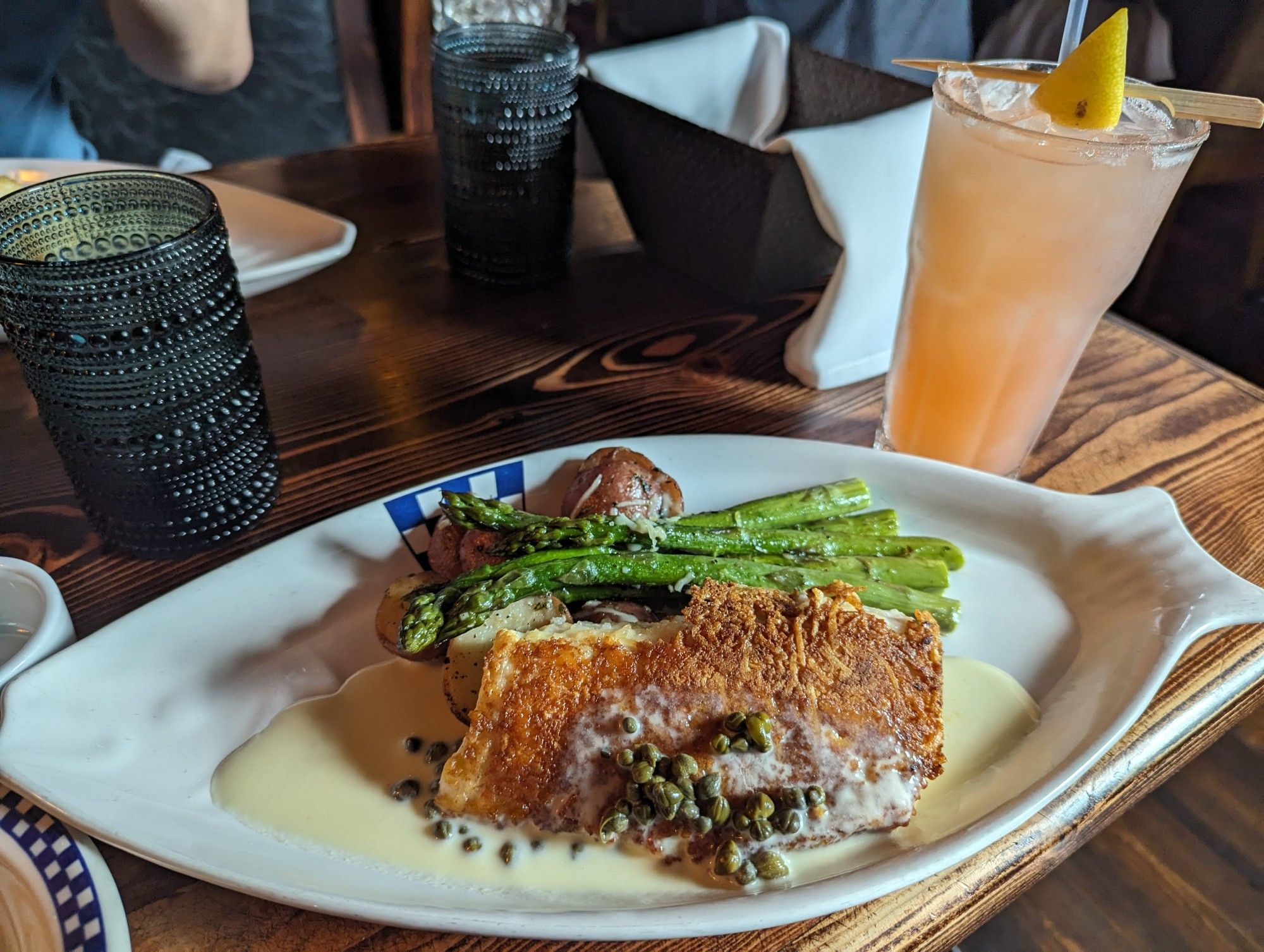 A plate of fish, asparagus, and potatoes on a table with several beverage glasses in the background