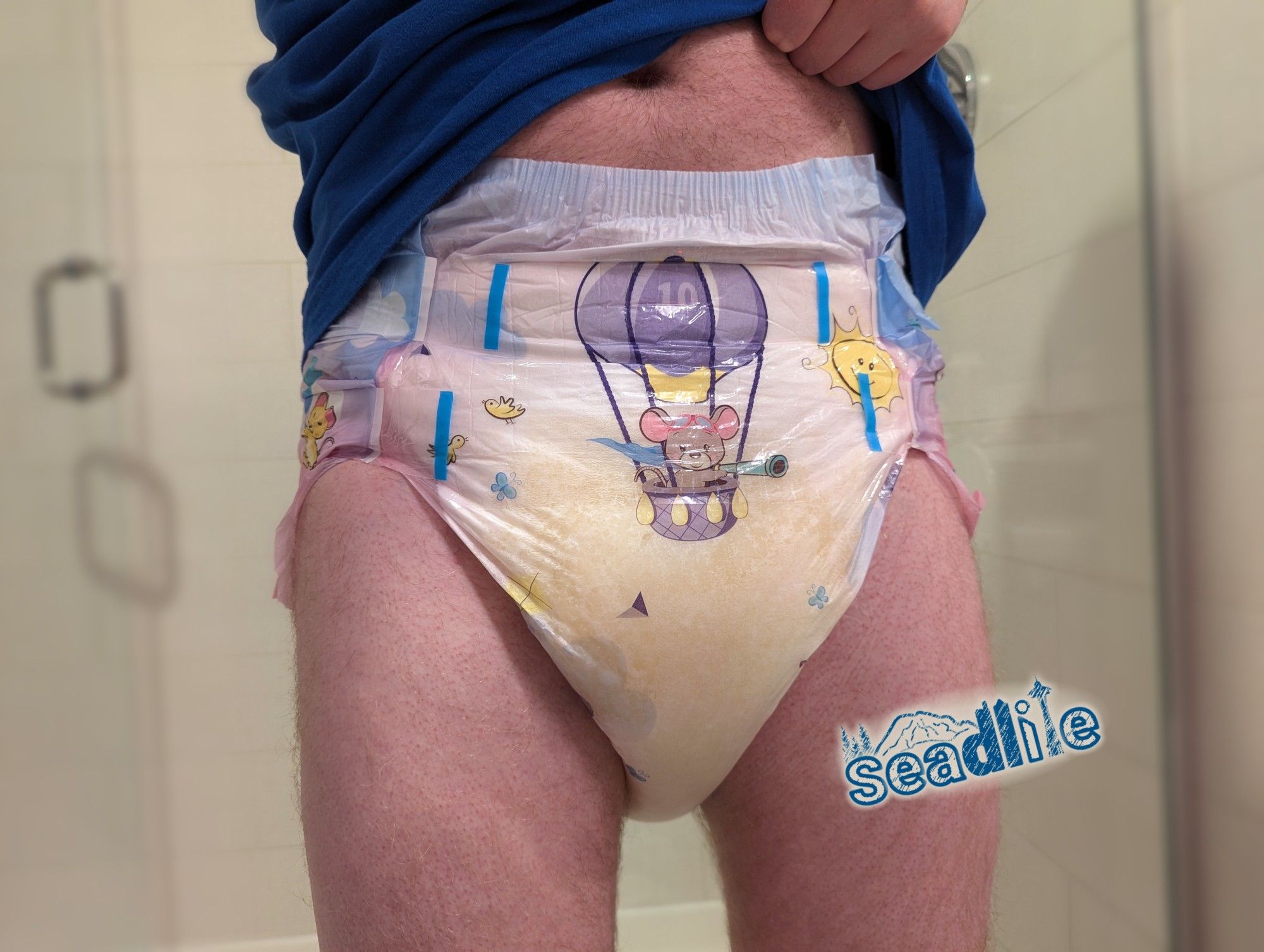 A man standing lifting up a blue t-shirt to show a wet Rearz Daydreamer diaper