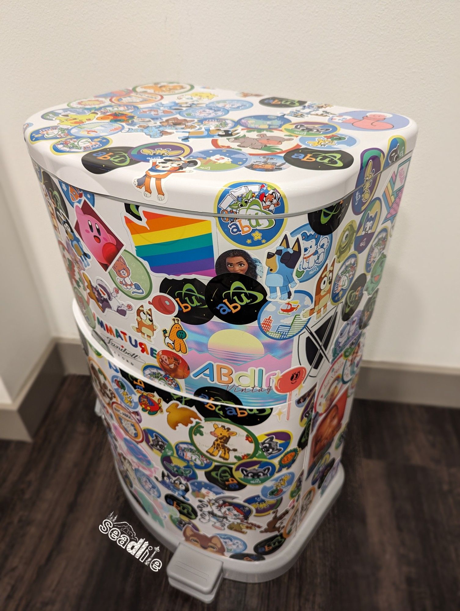 A Janibell Akord 330 diaper pail colored in colorful ABDL, babyfur, and cartoon stickers (right side perspective).