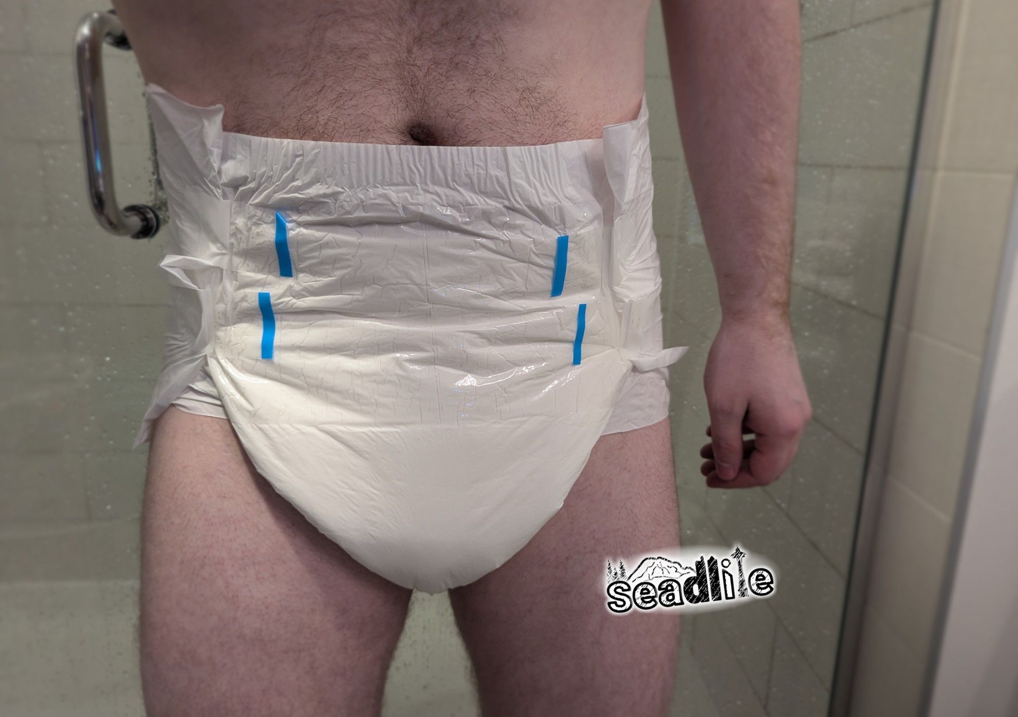 A man standing in front of a shower wearing a white adult diaper with 4 blue adhesive tapes