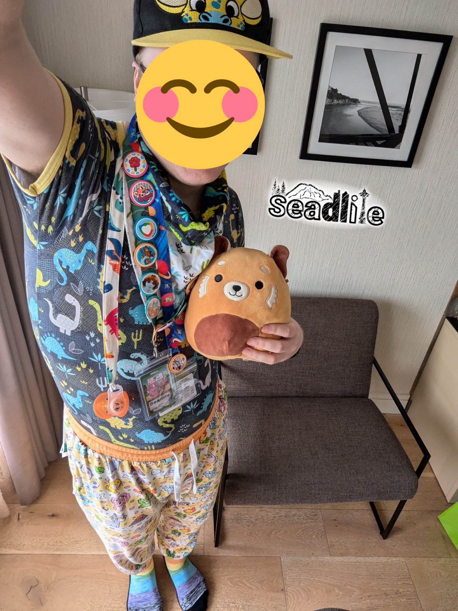 A man in a giraffe cap, dinosaur onesie, dinosaur PJs, and rainbow socks is standing with a red panda plushie. Also featuring a bandana, paci, con badge, and merit badge pins.