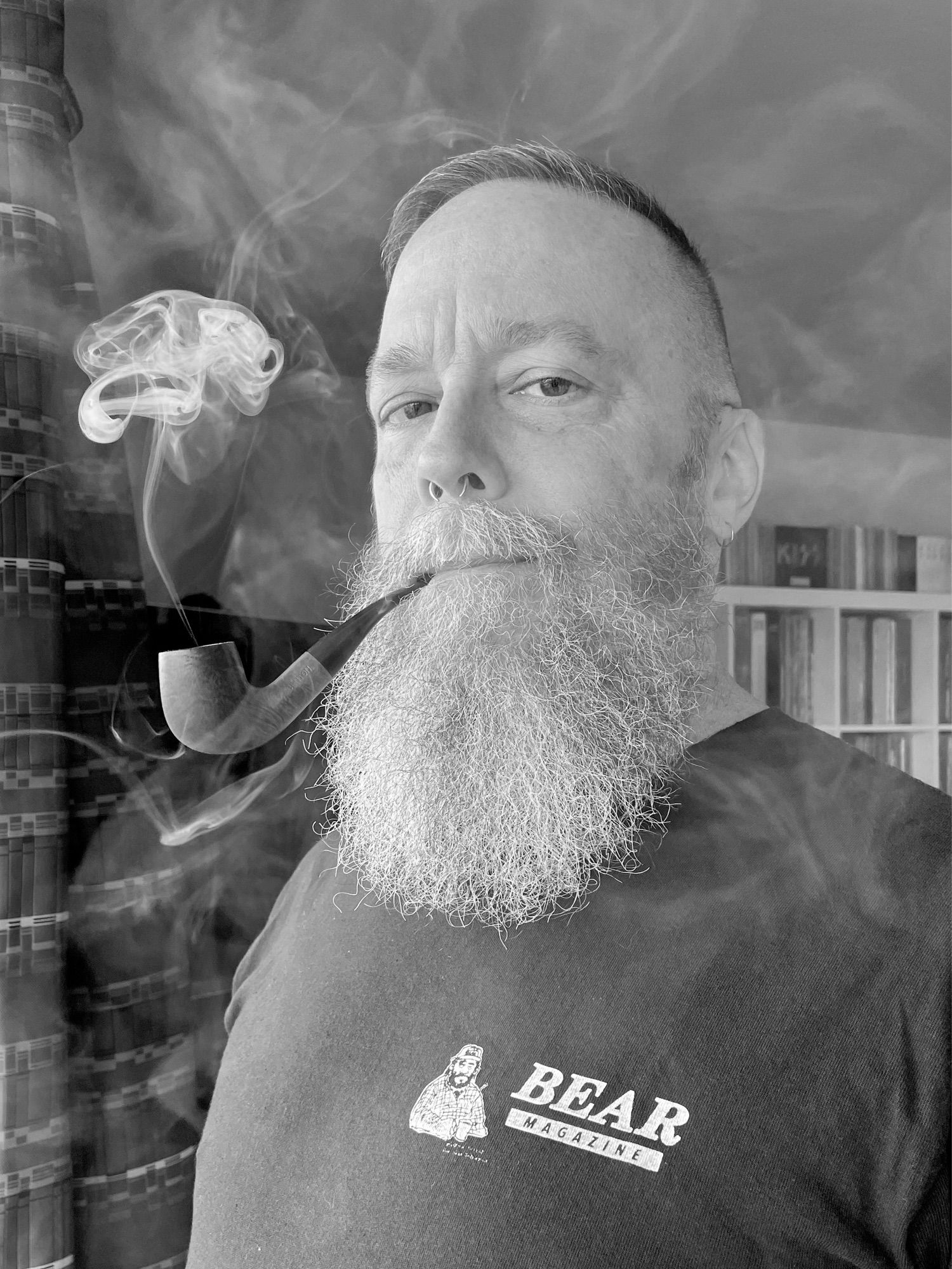 Black and white photo of me wearing a repro vintage Bear Magazine t-shirt and smoking my pipe, without my glasses again.