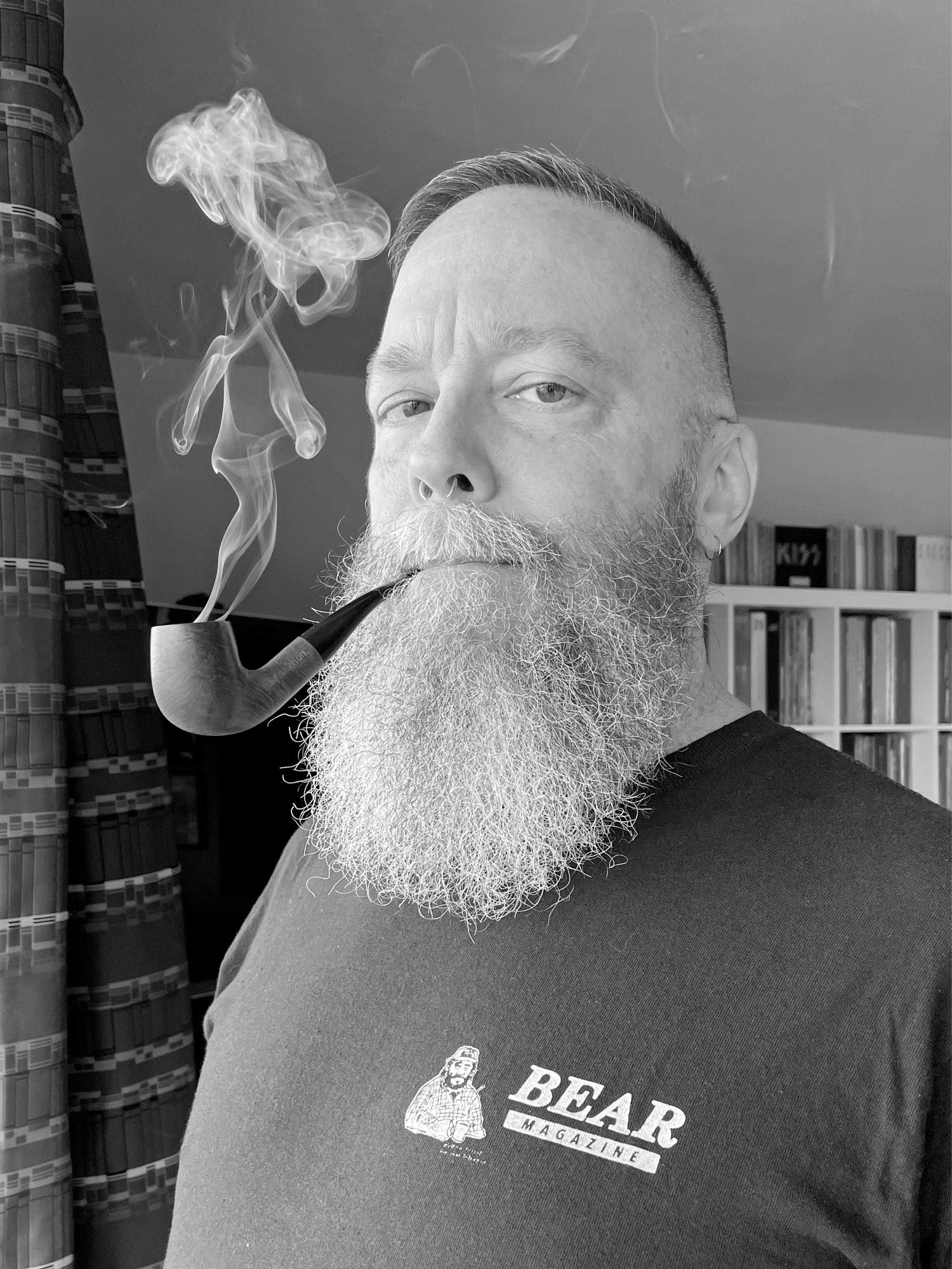 Black and white photo of me wearing a repro vintage Bear Magazine t-shirt and smoking my pipe, without my glasses.