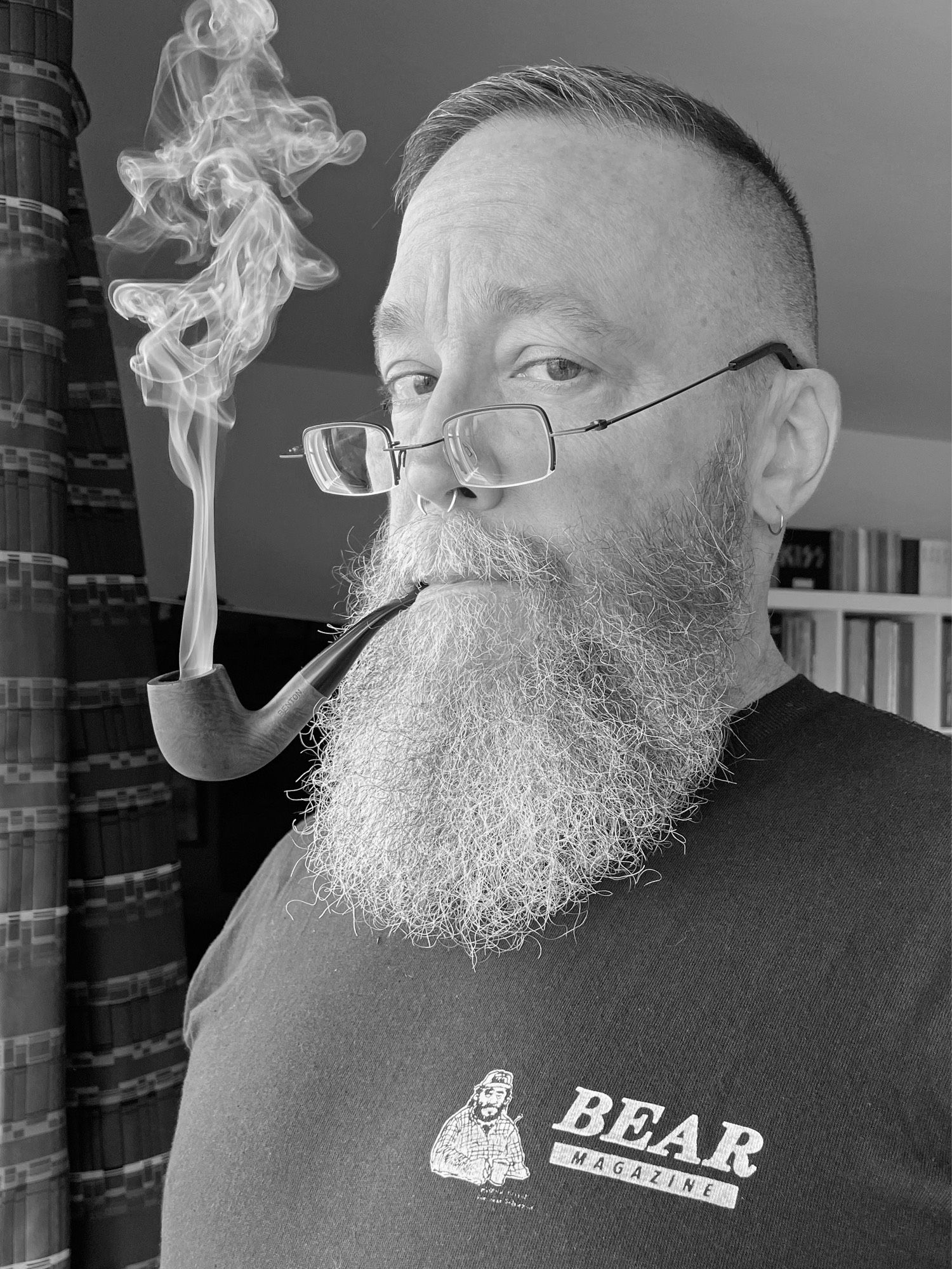 Black and white photo of me wearing a repro vintage Bear Magazine t-shirt and smoking my pipe as I look over the top of my glasses in a very judge-y dad kinda way.