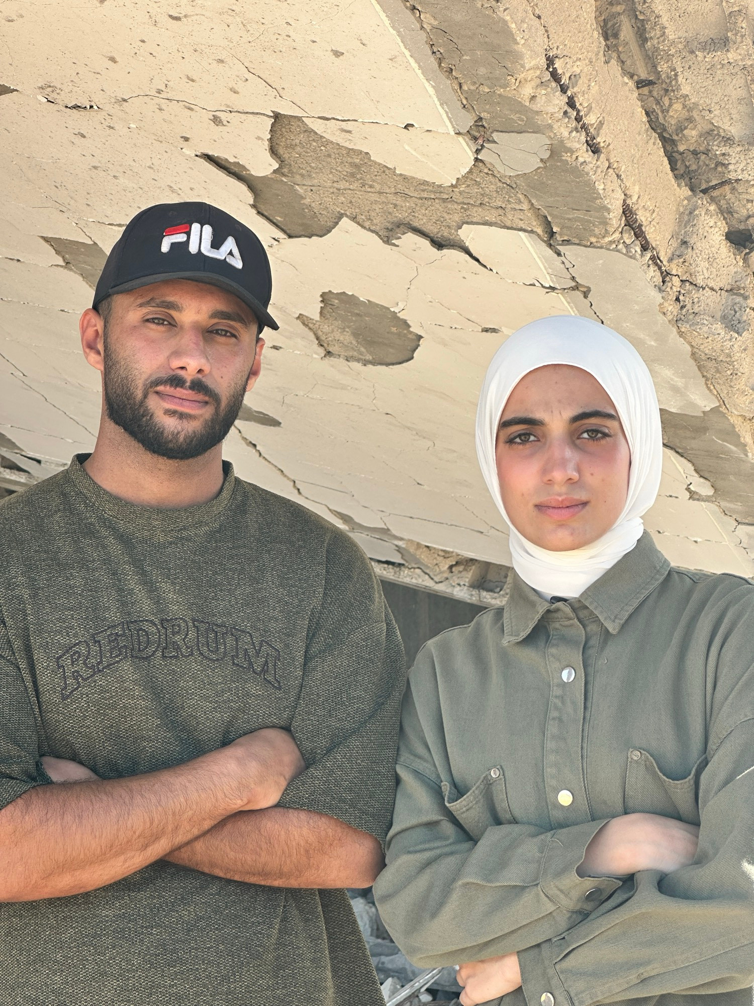 A young man and woman from Gaza sit side by side. Their faces are calm but deeply sad, as if carrying the weight of too many silent tragedies. They are close, holding on to each other for strength. The background is muted, reflecting a heavy emotional atmosphere. The photo speaks of quiet resilience, love, and deep pain.