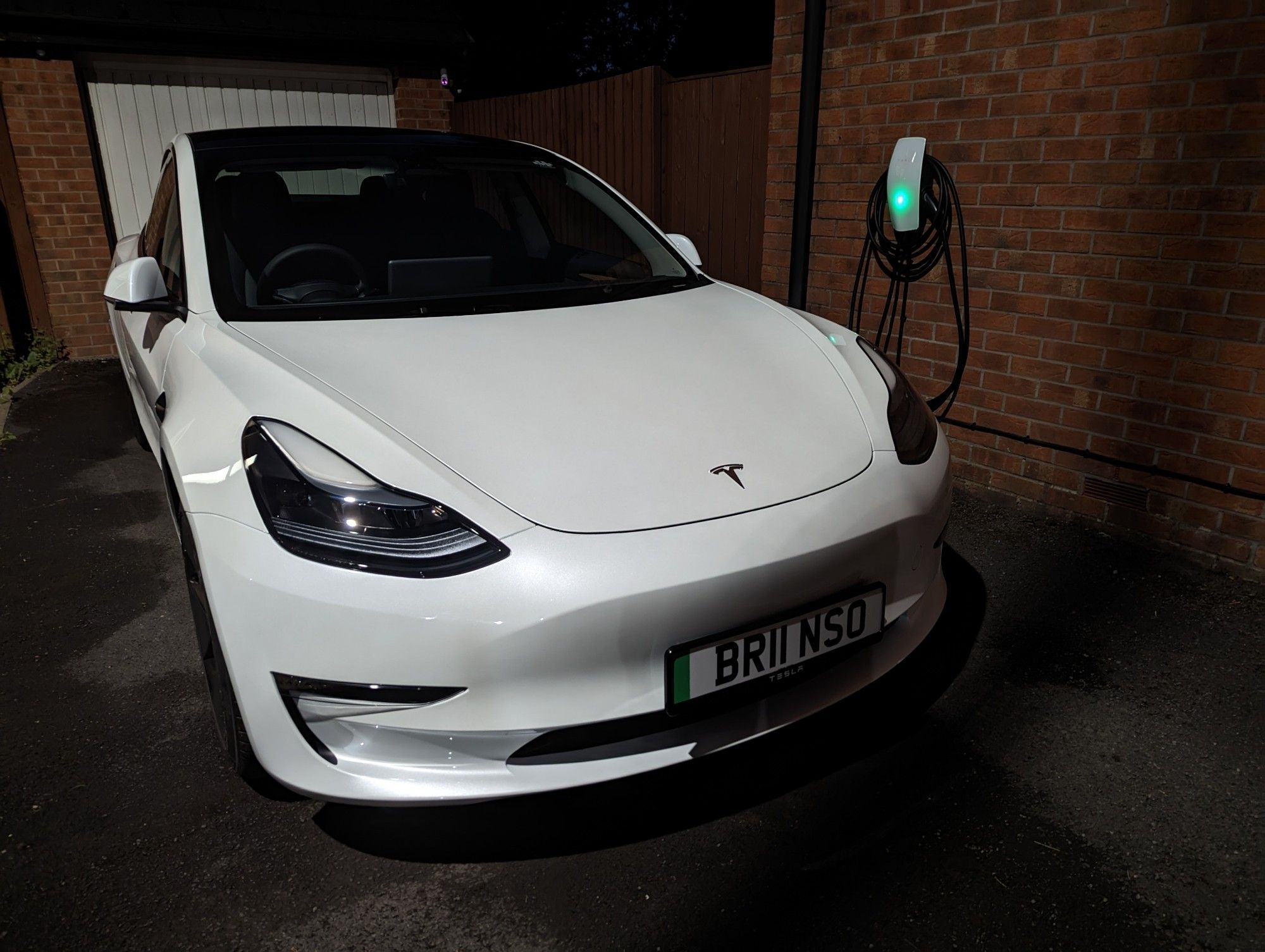 Photo of a white Tesla model 3 in the dark on a driveway, the front right of the car is the focal point.