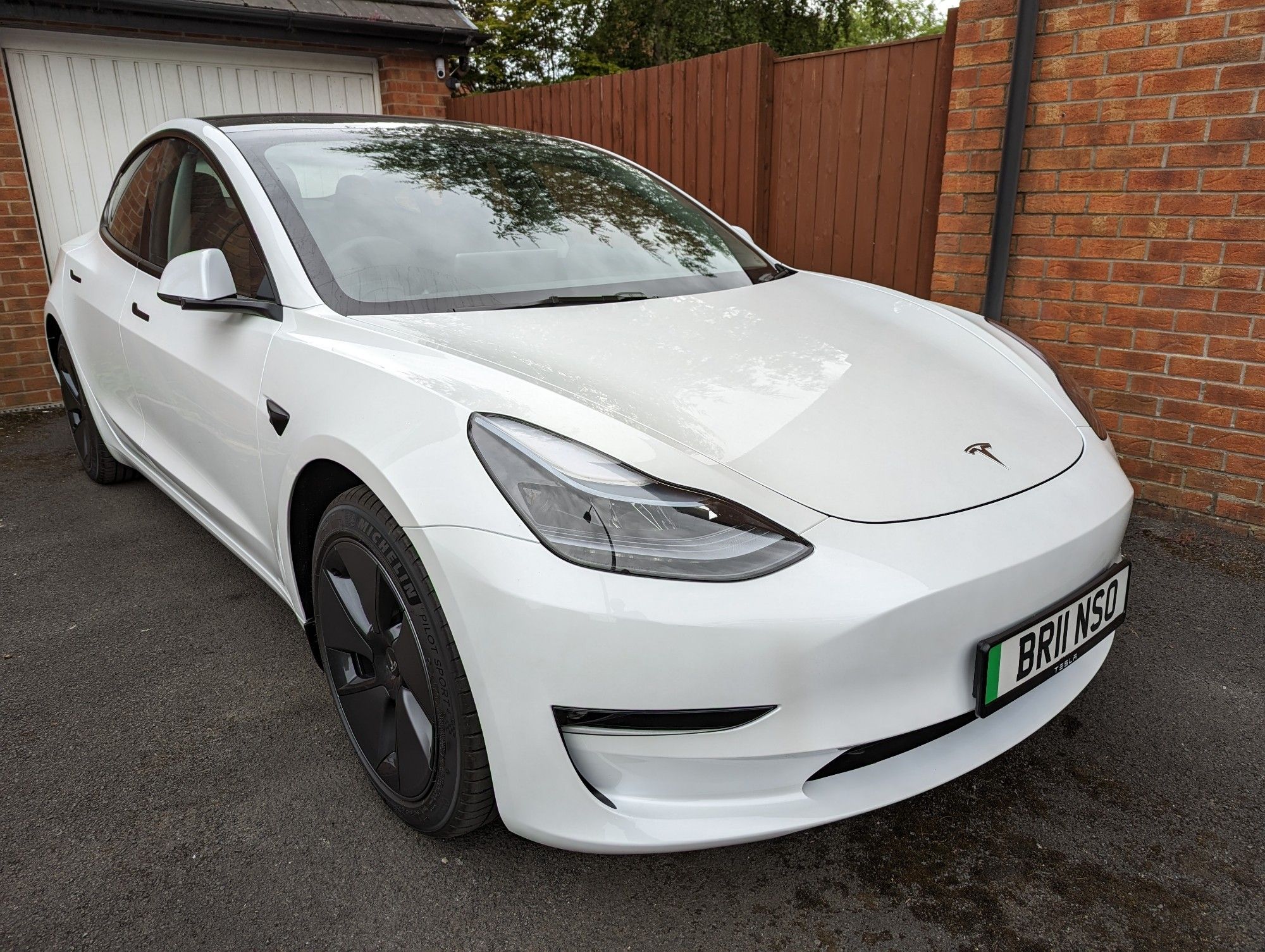 Photo of a white Tesla model 3 in the day time on a driveway, the front right of the car is the focal point.