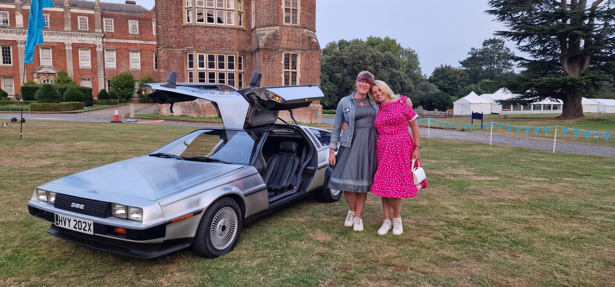 Rachel wearing a green 50's dress and Phoebe wearing a pink 50's dress standing next to a delorean 