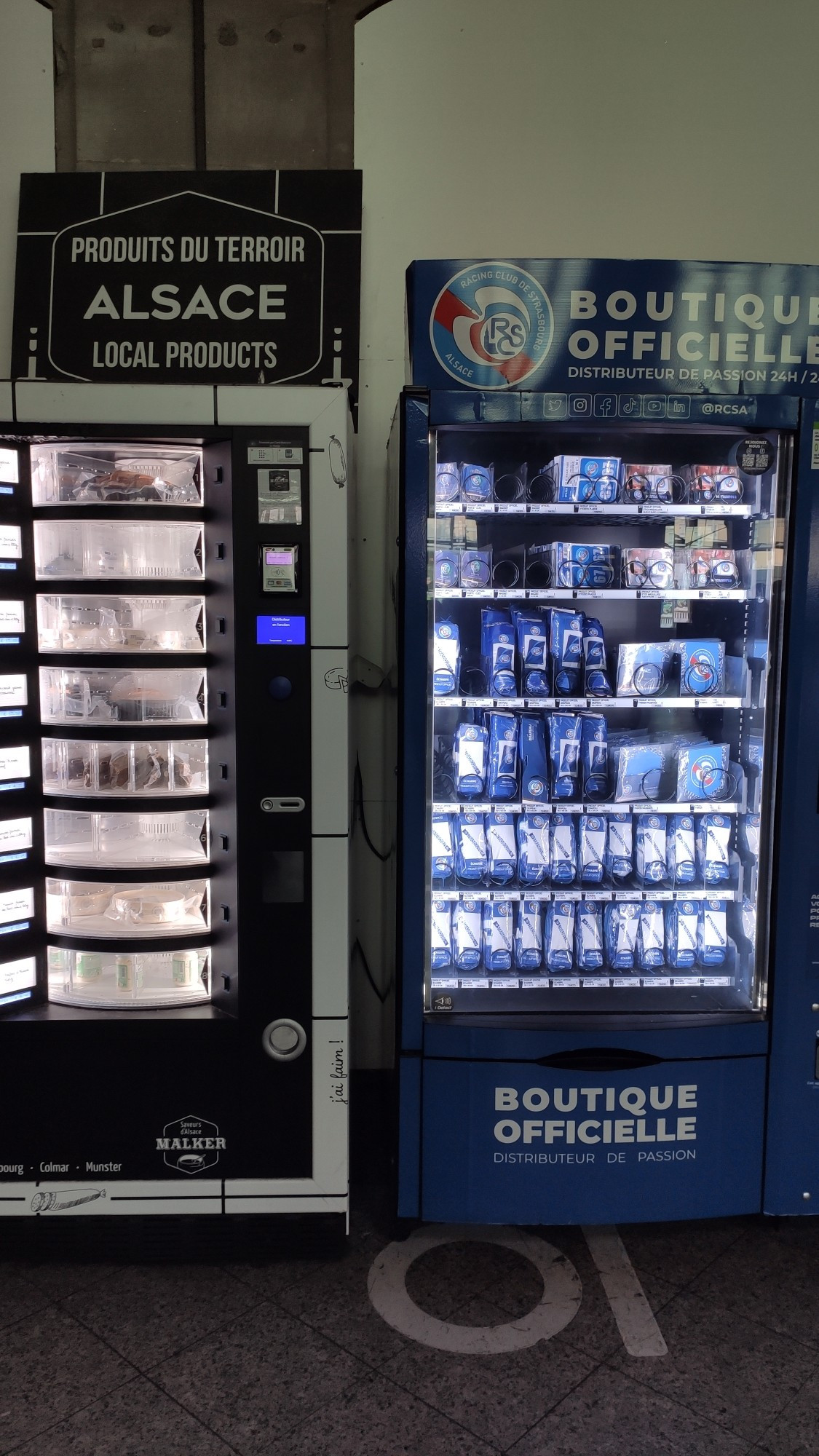 Photo de deux distributeurs automatiques. À gauche un distributeur noir "produits du terroir" qui vend de la choucroute et du munster et à gauche un distributeur bleu "boutique officielle" qui vend des produit dérivés du RCSA 