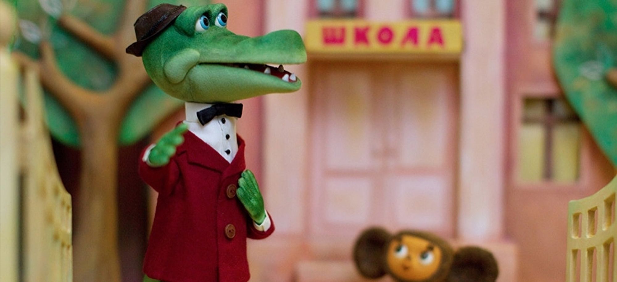 A gentlemanly russian crocodile in a red jacket and black hat in stop motion animation. He takes care of a little whatever called cheburashka