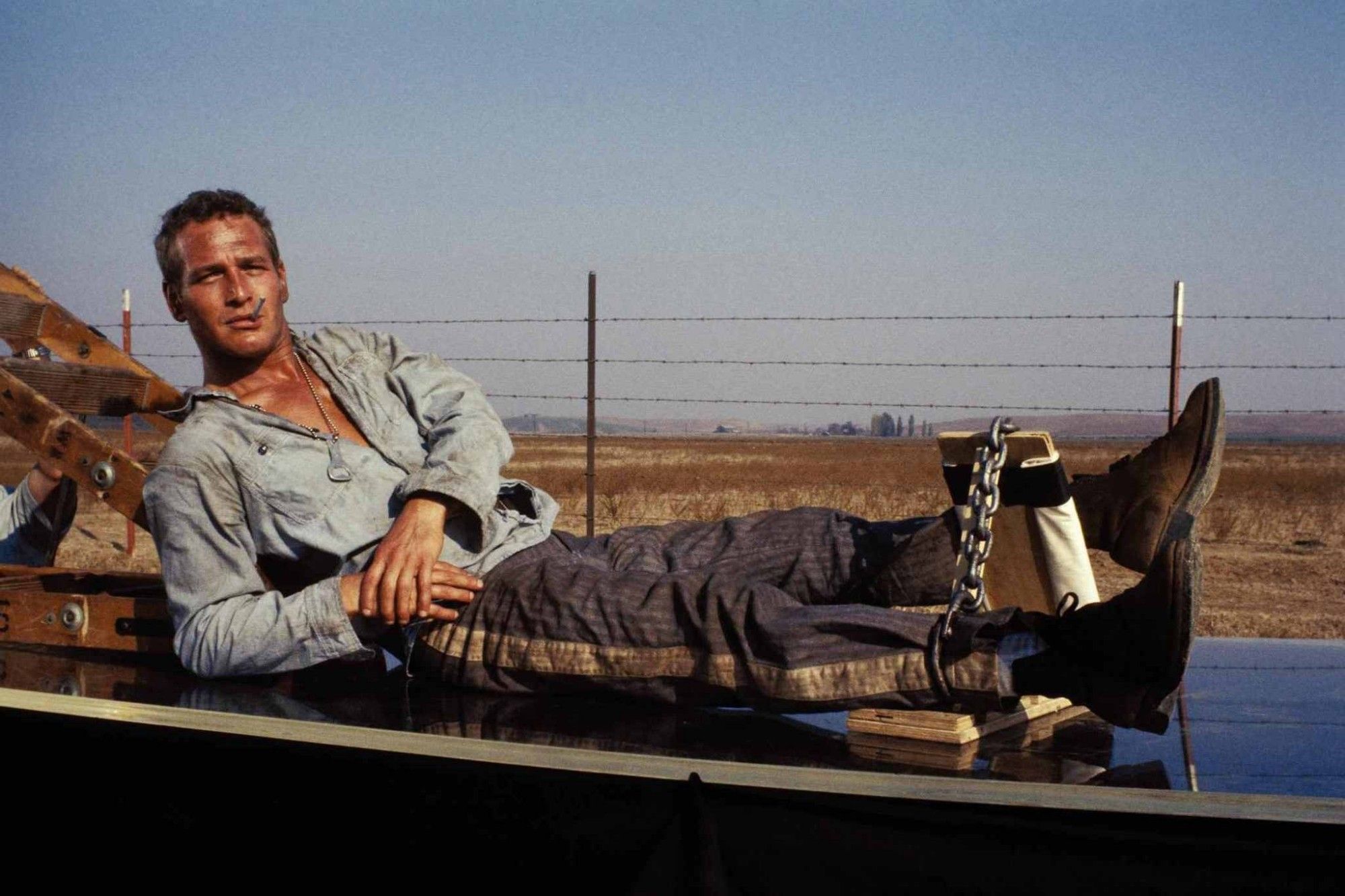 Paul Newman from cool hand Luke, his is a white man with a cigarette in his mouth and chains on his ankles, resting in his blue prison uniform