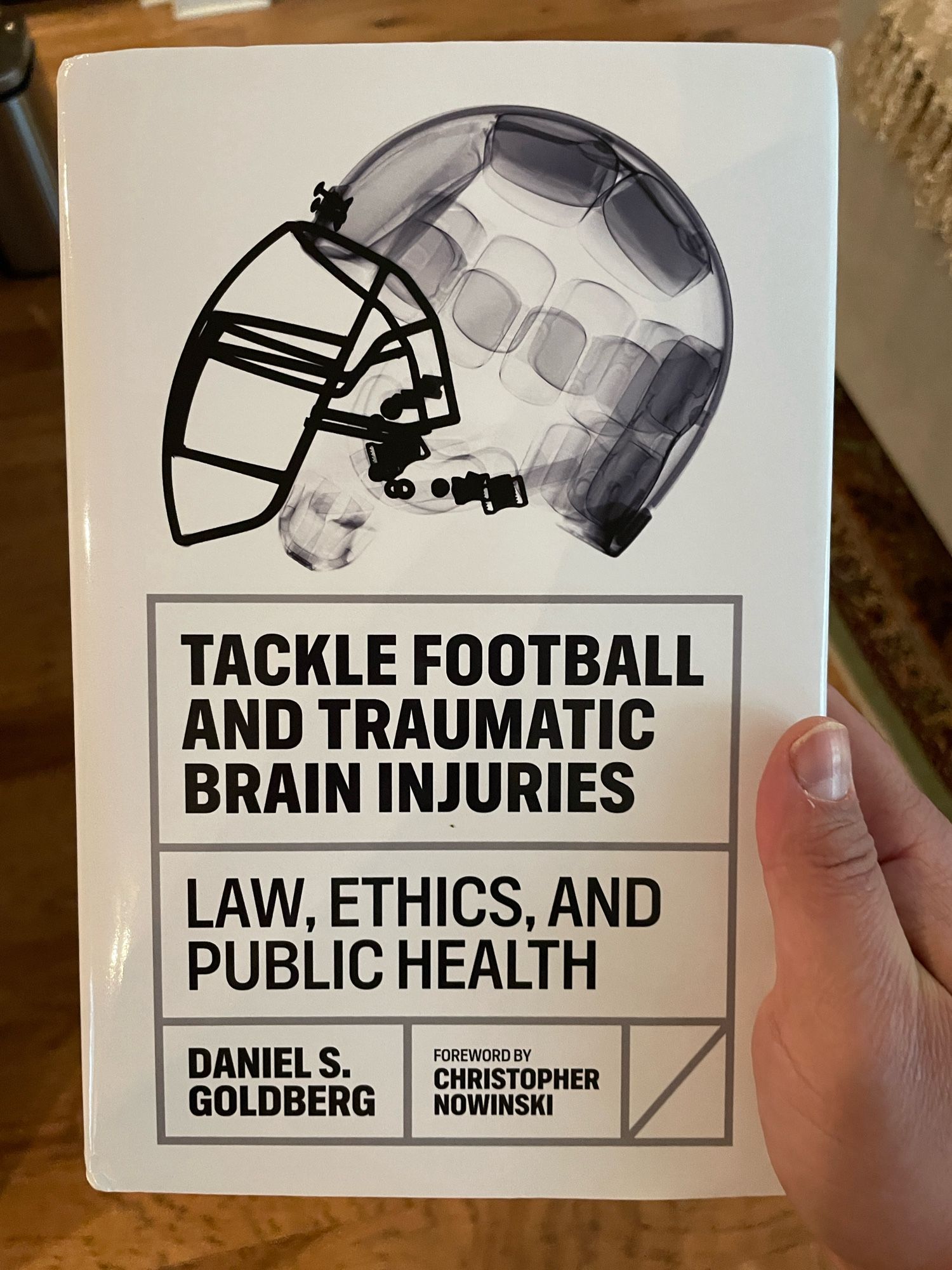 Top down shot of a man holding a book entitled “Tackle Football and Traumatic Brain Injuries: Law, Ethics and Public Health”