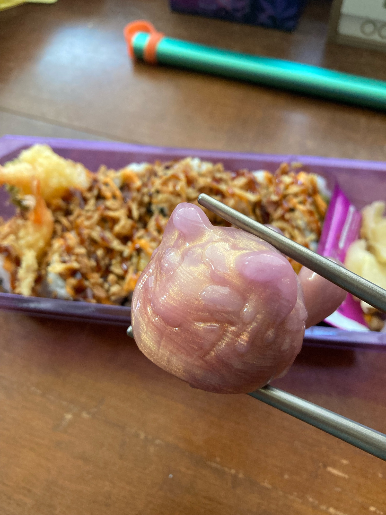 A pair of titanium chopsticks hold an adorable, shimmery Squish kit from @hodge-podge.bsky.social. A box of tempura sushi sits in the background waiting to be eaten.