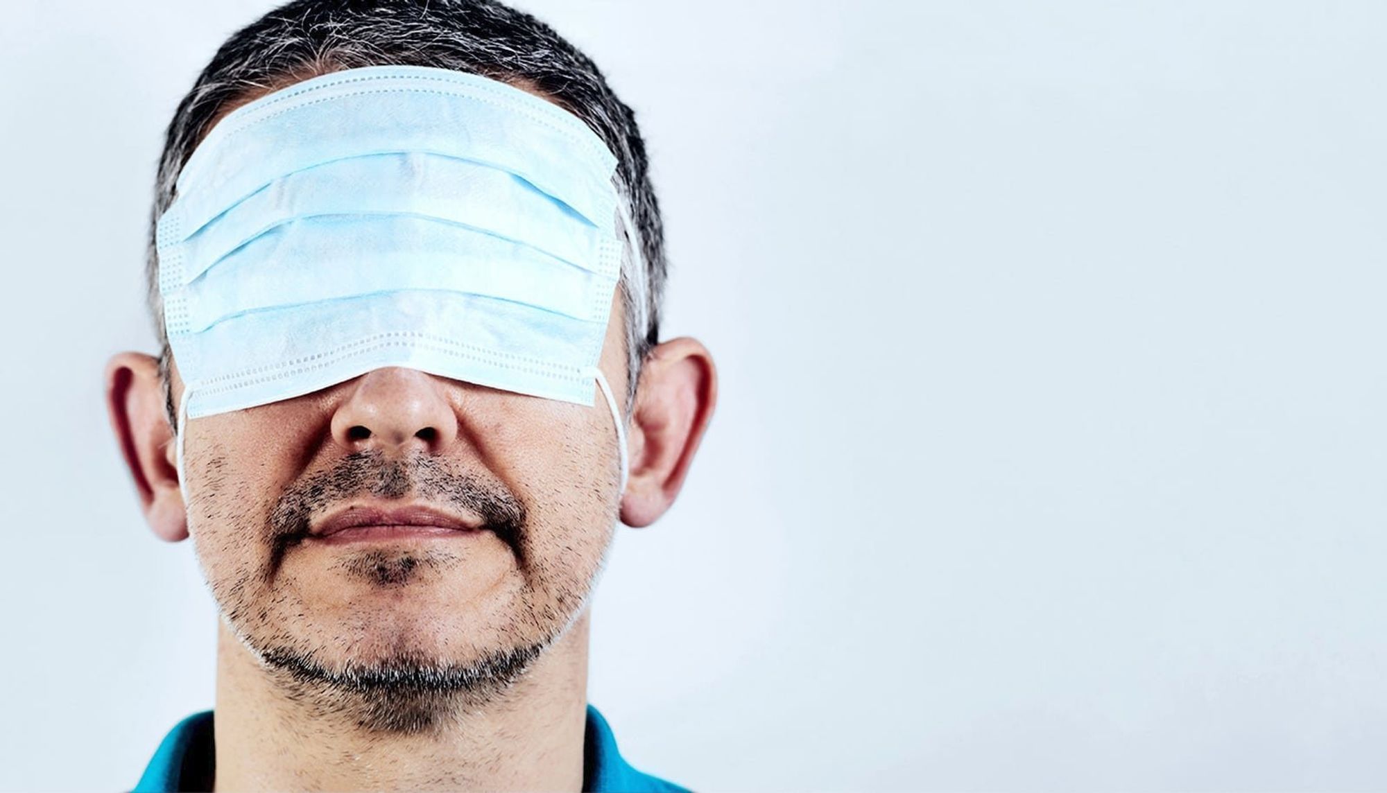 A man wearing a medical mask as a blindfold.