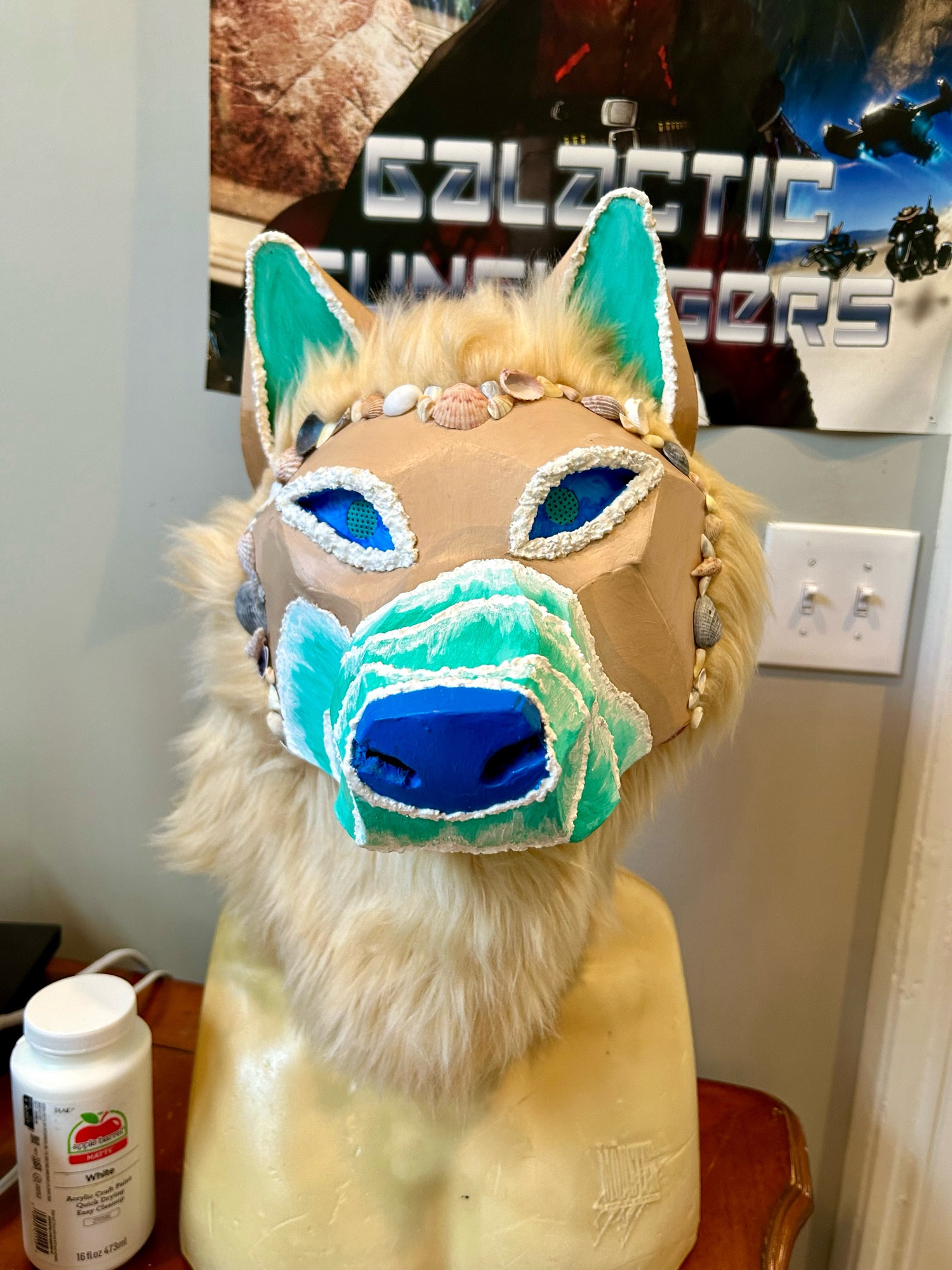 A photo of a beach themed fursuit head. The mask is painted and has real shells. The fur flows like sand