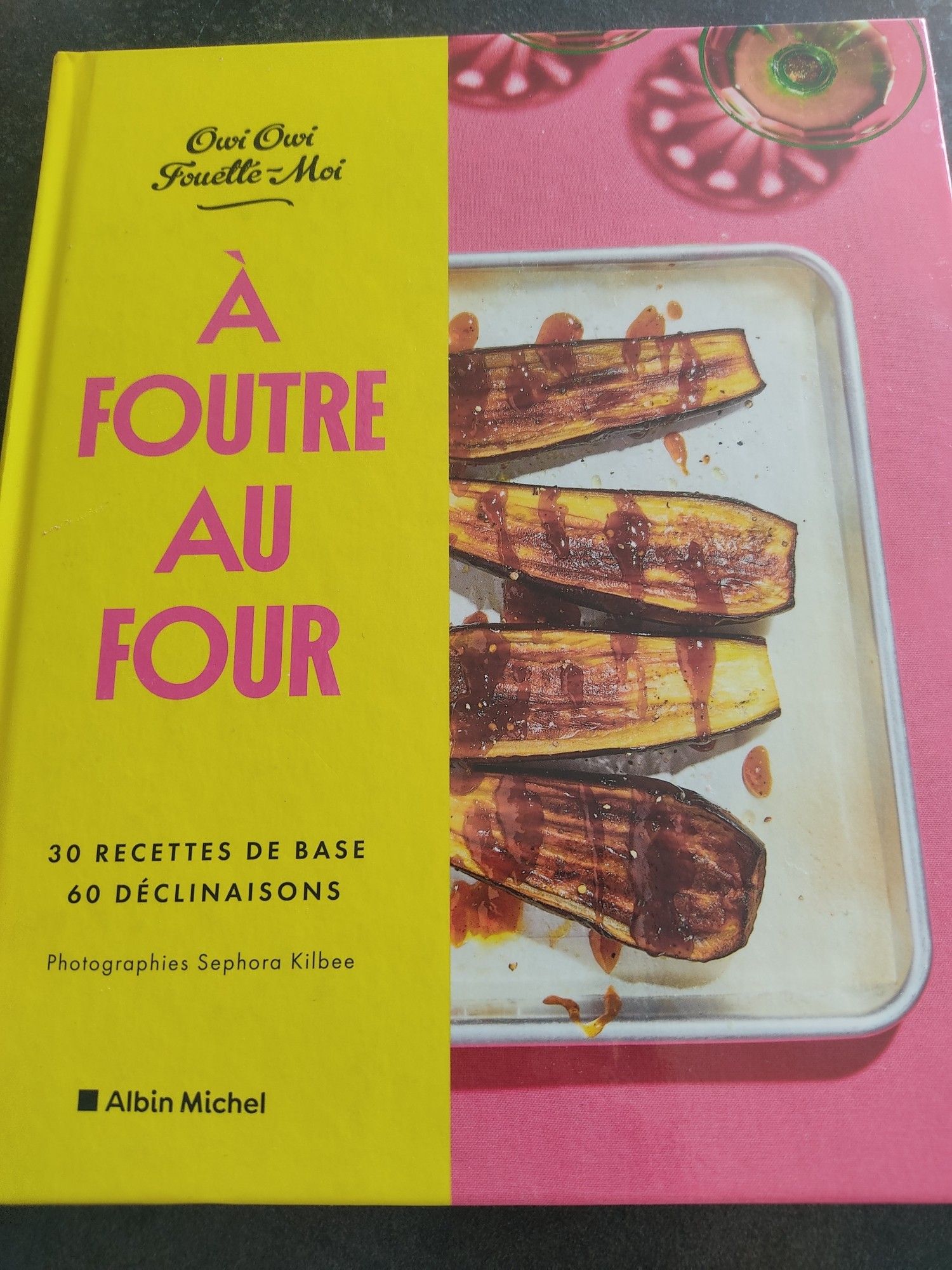 Photo de couverture du livre À foutre au four d'OwiOwi Fouette-Moi, la moitié gauche a un fond jaune avec le titre écrit en rose et sur la moitié droite on peut voir 4 demies aubergines rôties au four.