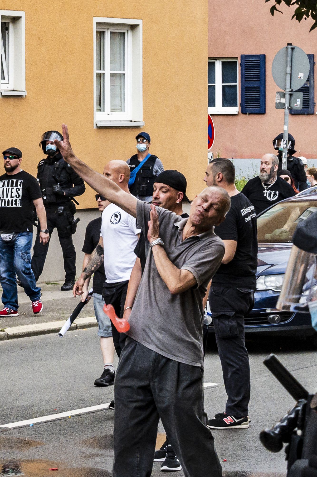 glatzköpiger älterer Neonazi Christian Worch in grauem Poloshirt hebt die Hände zur Abwehr von Wasserbomben. 
Eine rote Wasserbombe trifft ihn an der Hüfte. Im Hintergrund weitere Neonazis