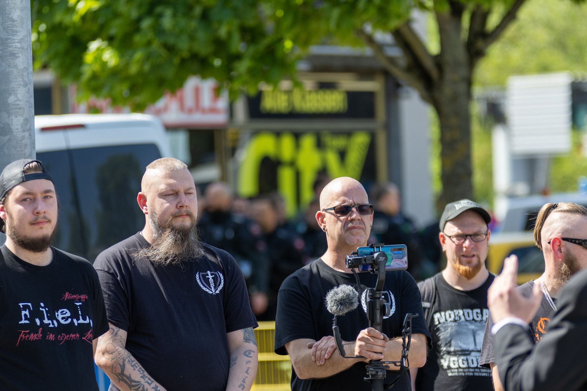 Mehrere Neonazis stehen in einer Reihe und hören einem Redebeitrag zu