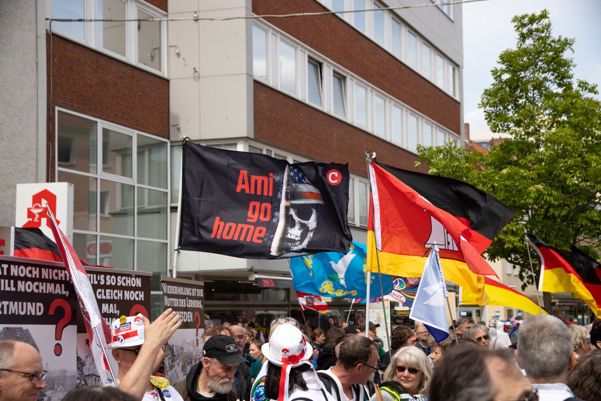 Unten im Bild Kopfe der TeilnehmerInnen unter einem Fahnenmeer; eine "Ami go home" Fahne des extrem rechten 'Compact' Versand