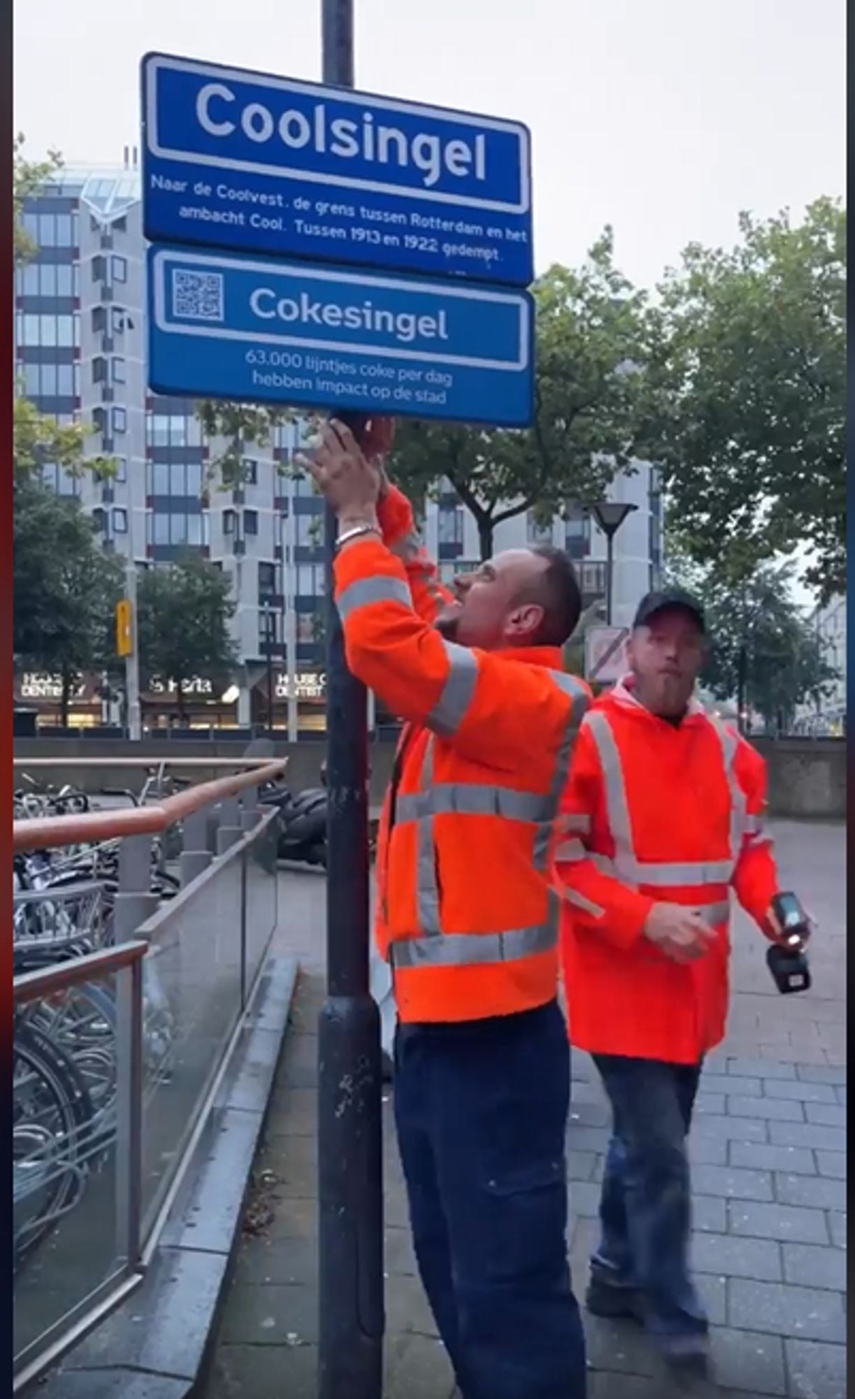 Two workers putting a sign with "Cokesingel" underneath the "Coolsingel" street sign