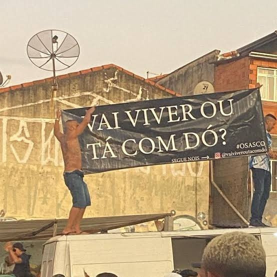 foto de dois homens segurando uma faixa com a frase "vai viver ou tá com dó?"