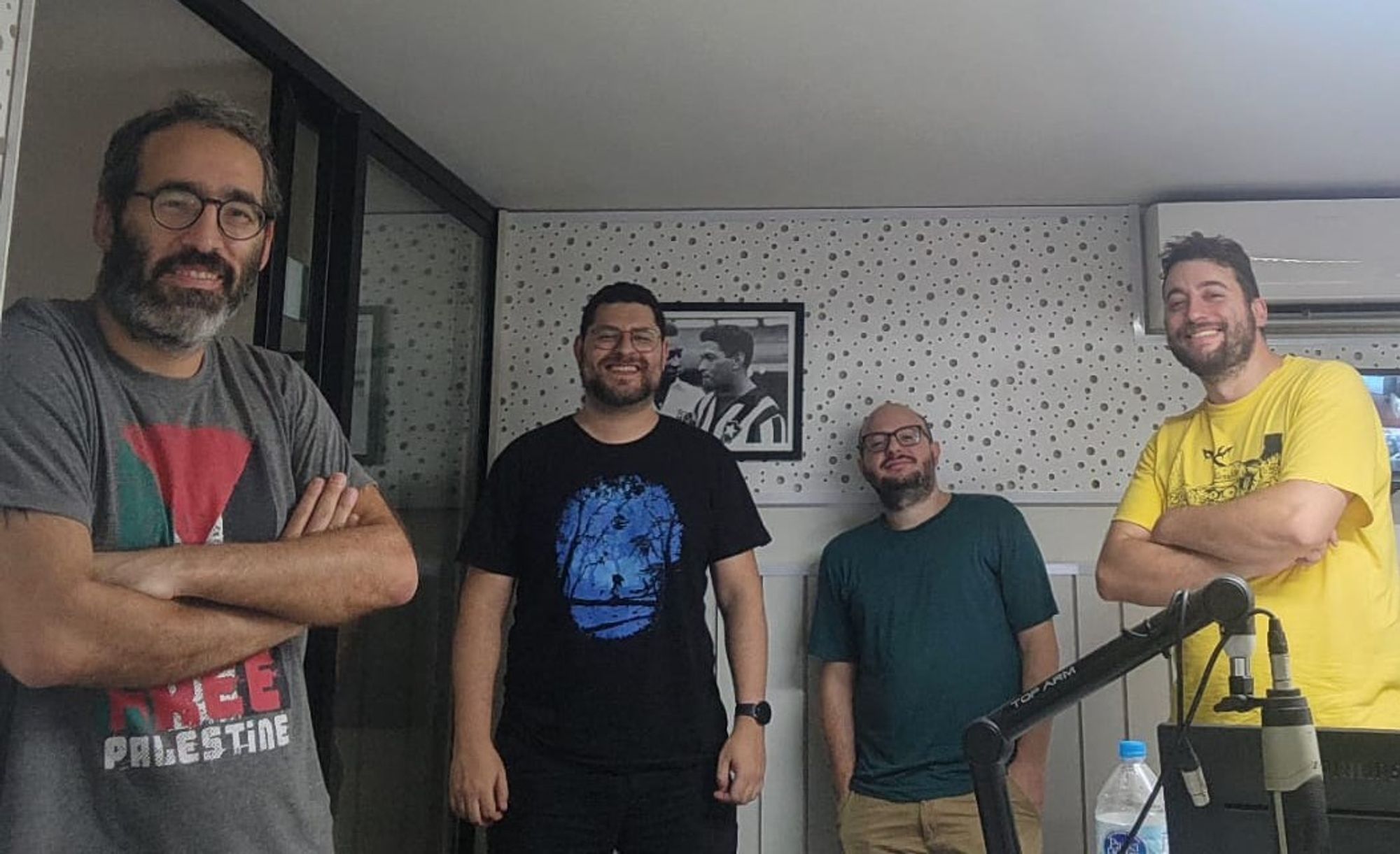 Quatro homens olhando para a câmera, dentro de um estúdio de gravação de podcasts