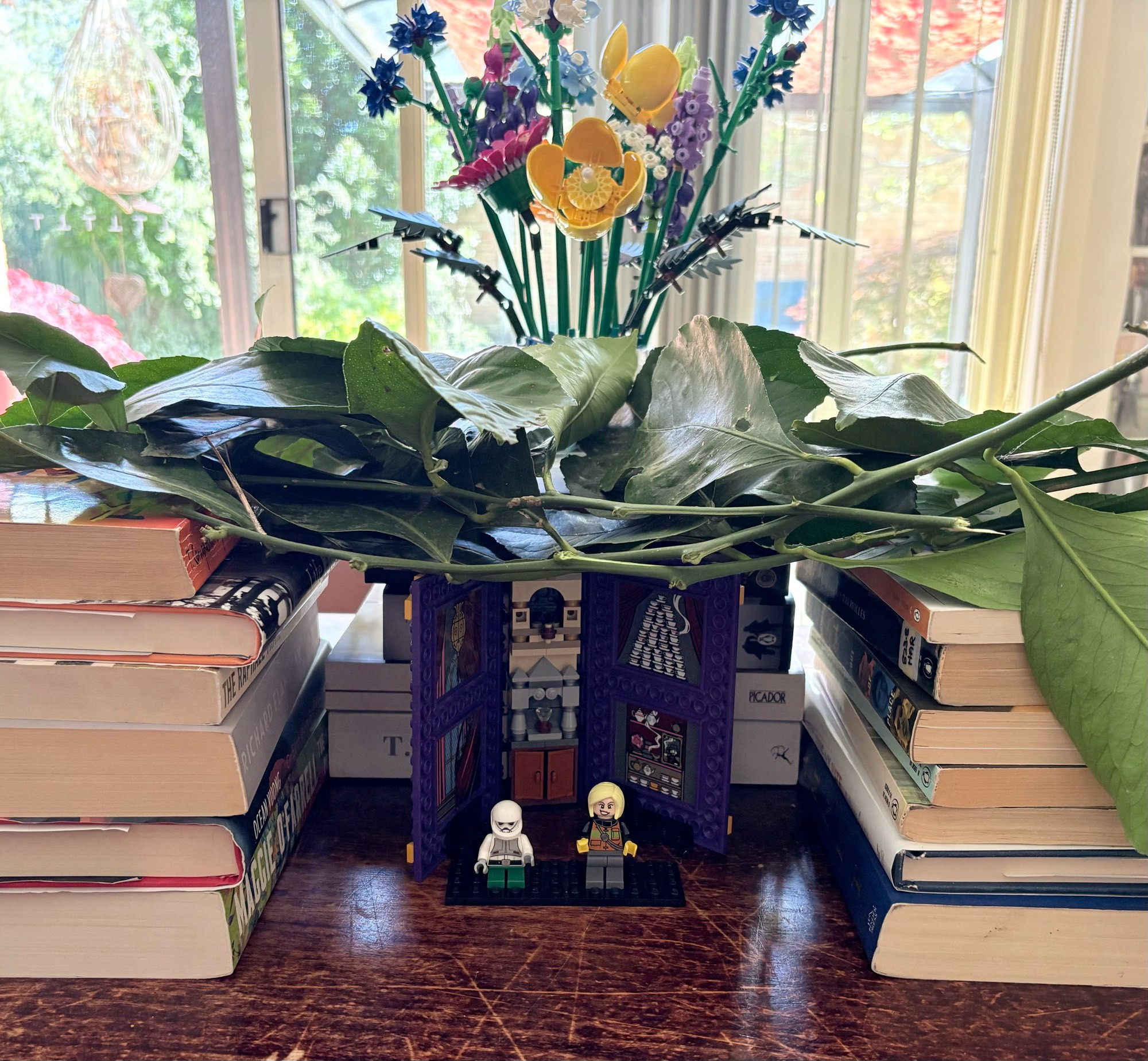 A small sukkah made of books and branches of a lemon tree for the roof, with small Lego figurines inside. 