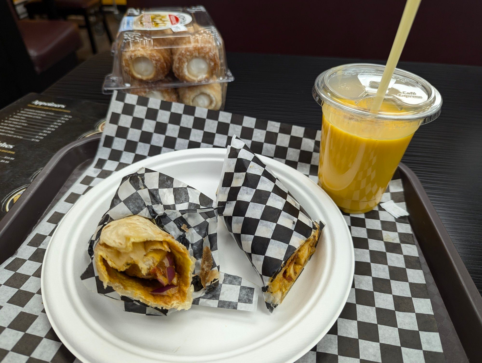 Said meal on tray with checkerboard parchment paper, with creme filled pastry in the background.