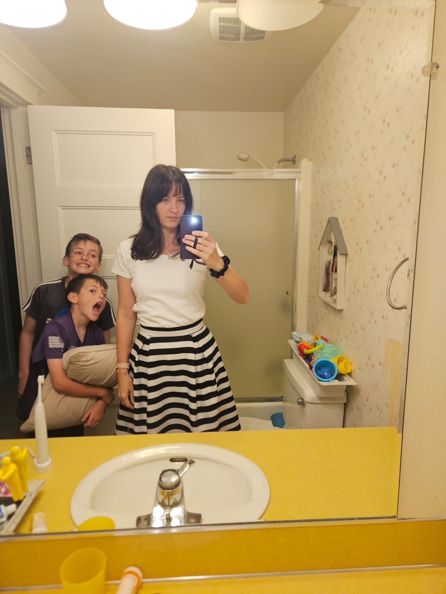 Picture in my bathroom mirror. I'm wearing a white fitted T-shirt and a black and white horizontal striped a-line skirt. Two of my children are being goofballs next to me.