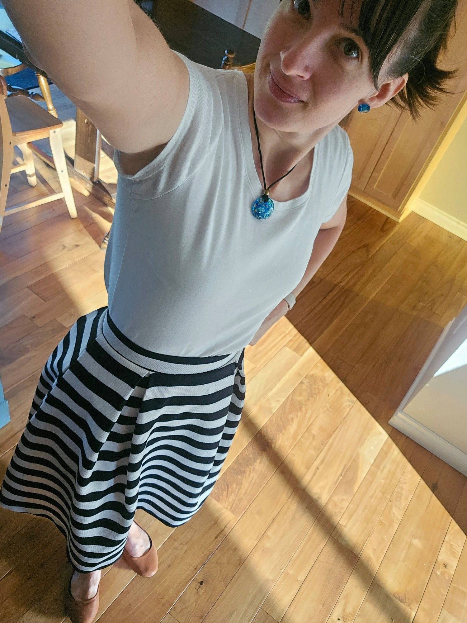 Whole body selfie of me in a cute black and white striped a-line skirt with fitted white tee, brown ballet flats and matching dark turquoise glass pendant necklace and earrings.