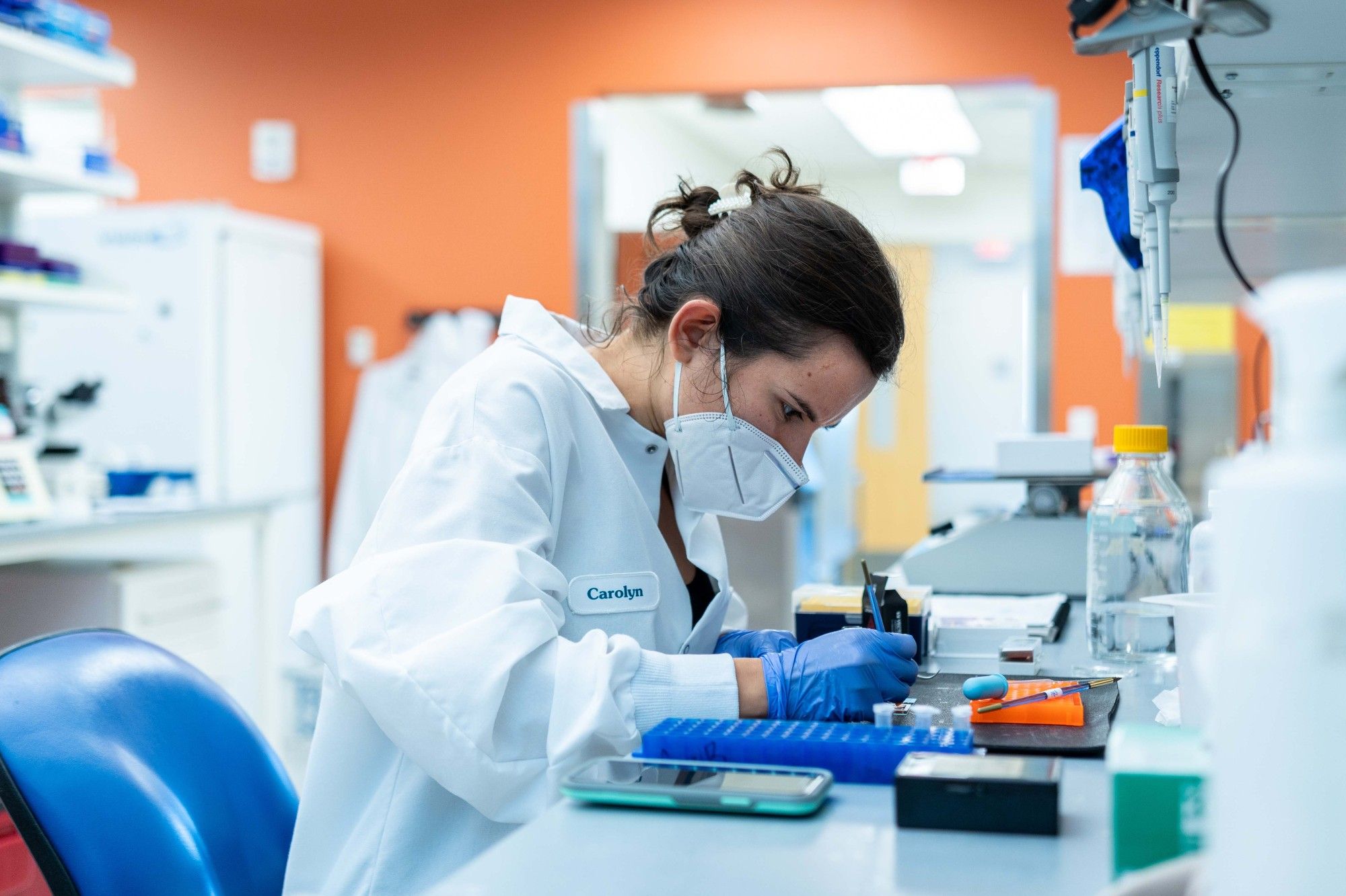 A female scientist with brown hair wearing a mask works in a lab