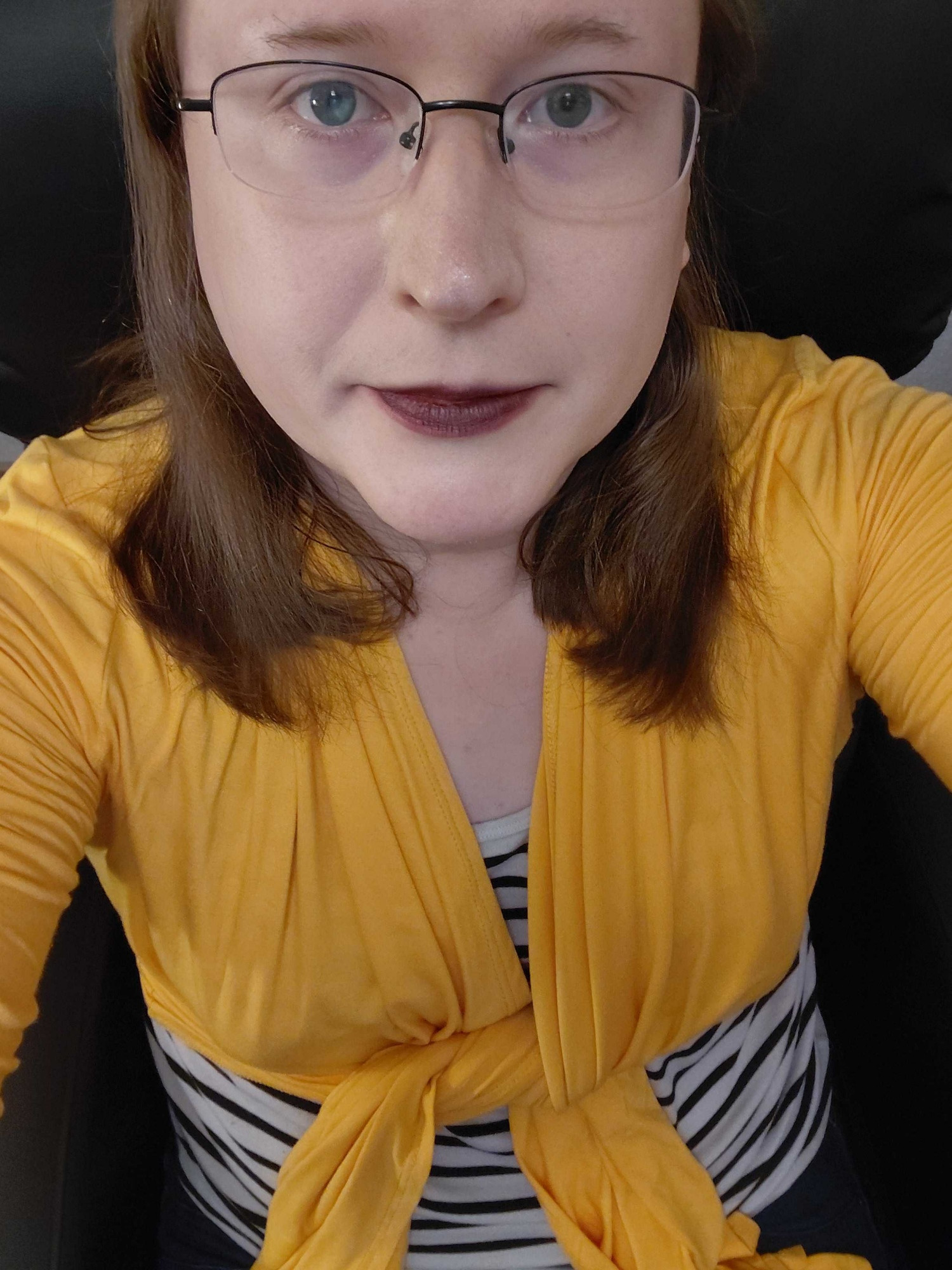 yellow jacket black and white striped top long brown hair glasses purple lipstick looking at camera sitting down. hot 