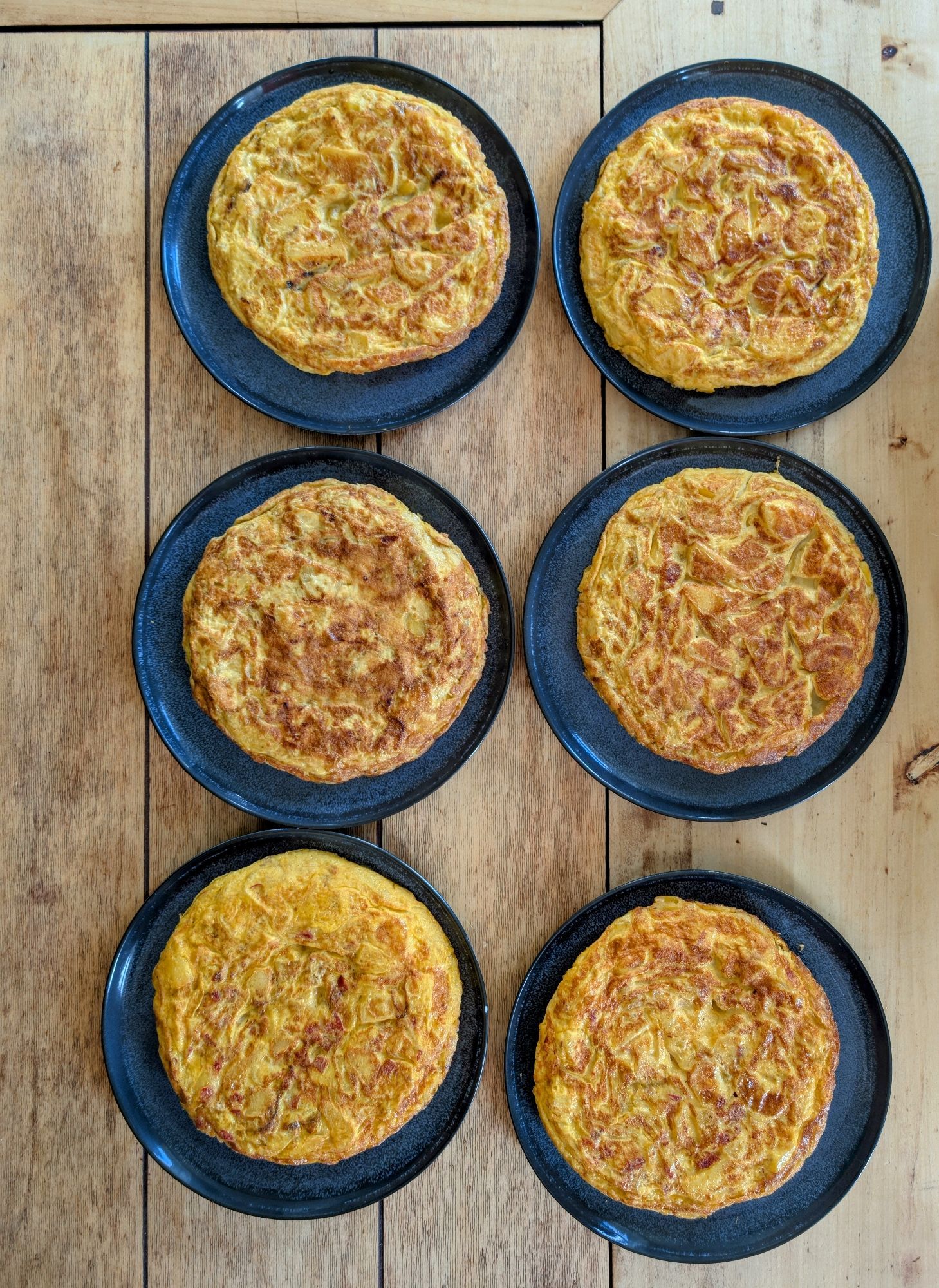 6 spanische Tortillas auf dunkelblauen Tellern. Durch das 20 minütige Vordämpfen der Erdäpfel, erspart man sich beim darauffolgenden Dünsten sehr viel Zeit. Zwei habe ich auf Wunsch mit Chorizo gemacht. Alle anderen sind klassisch.