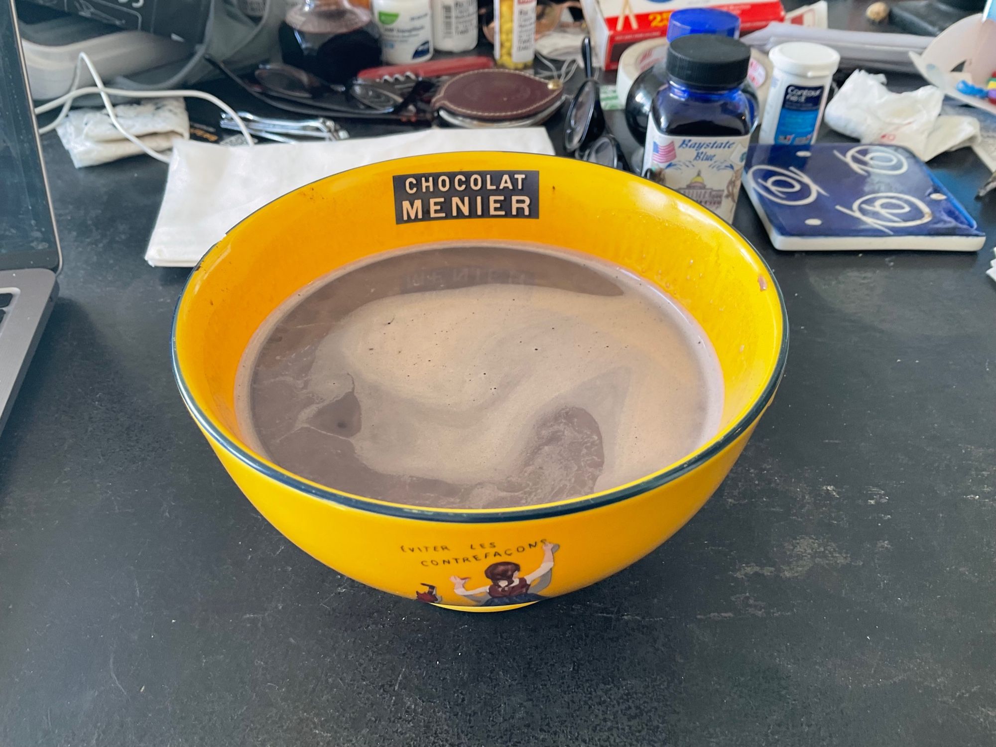 A yellow bowl with the CHOCOLAT MENIER logo filled with hot chocolate