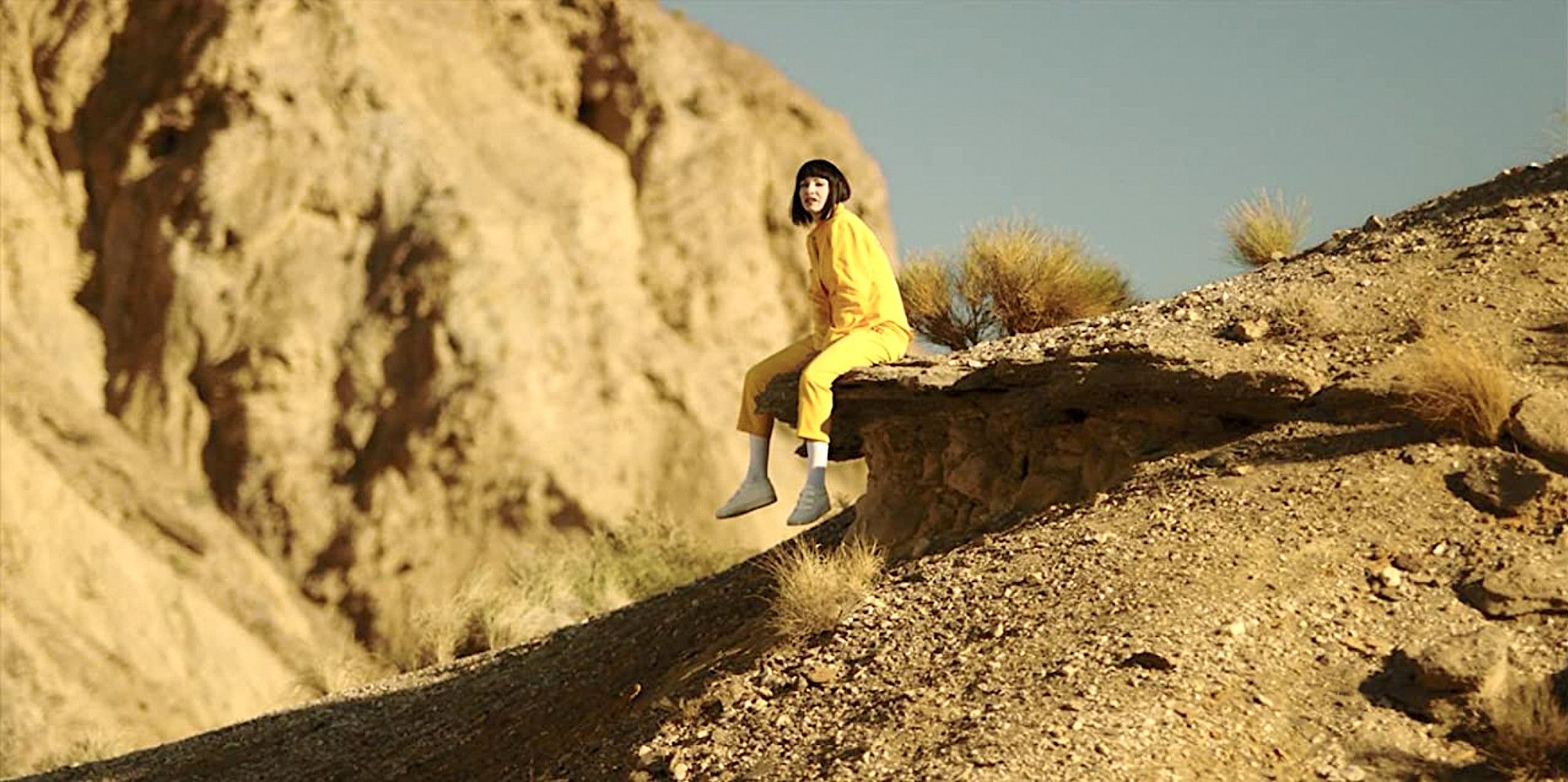 Najawa sitting on a rock in a yellow prison jumpsuit in desert landscape