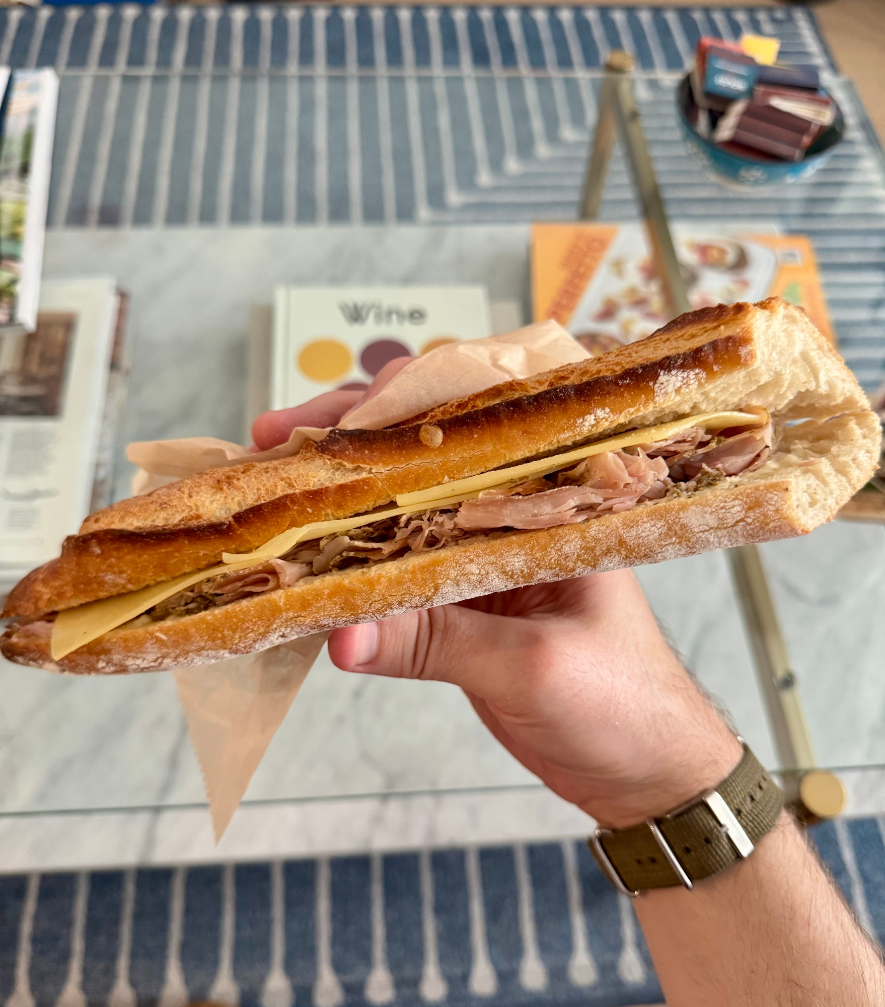 A man’s hand holding a ham and cheese baguette 