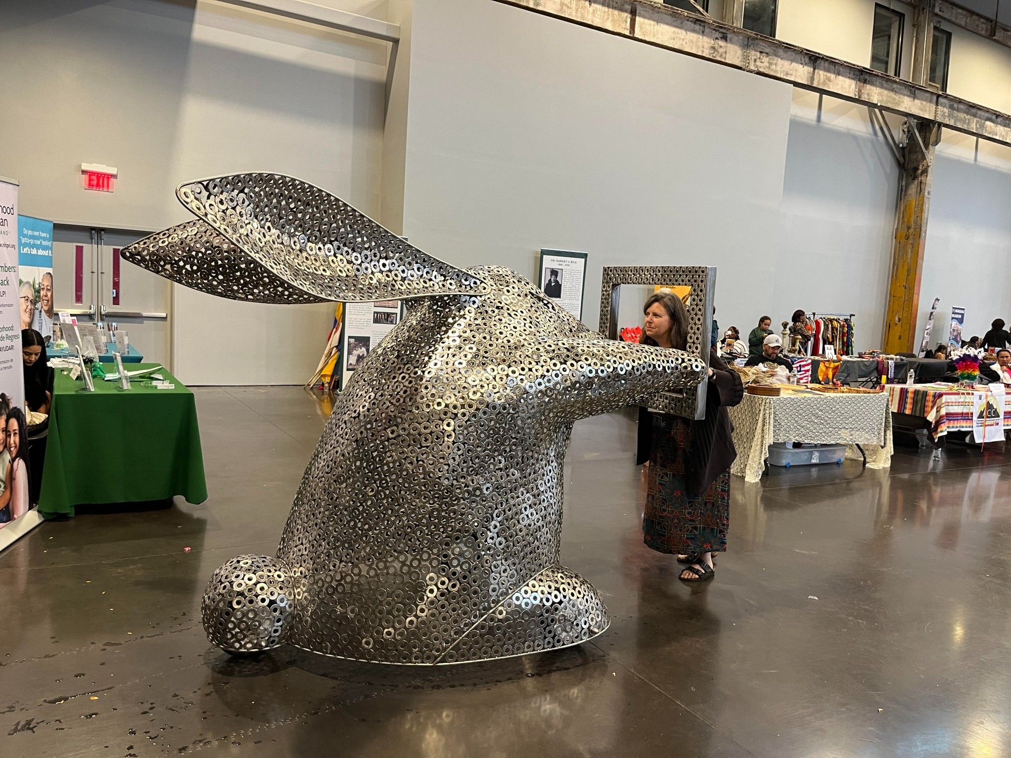 a metal rabbit, about five 1/2 feet tall, aggressively holds out an empty ,eta; frame at a medium sized woman who holds it right back from the other side, looking as aggressive as she can.